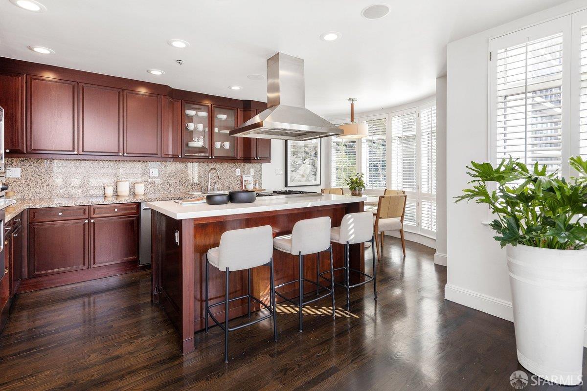 Kitchen with a cherry-wood island, bar stools, granite backsplash, and bright shuttered windows.