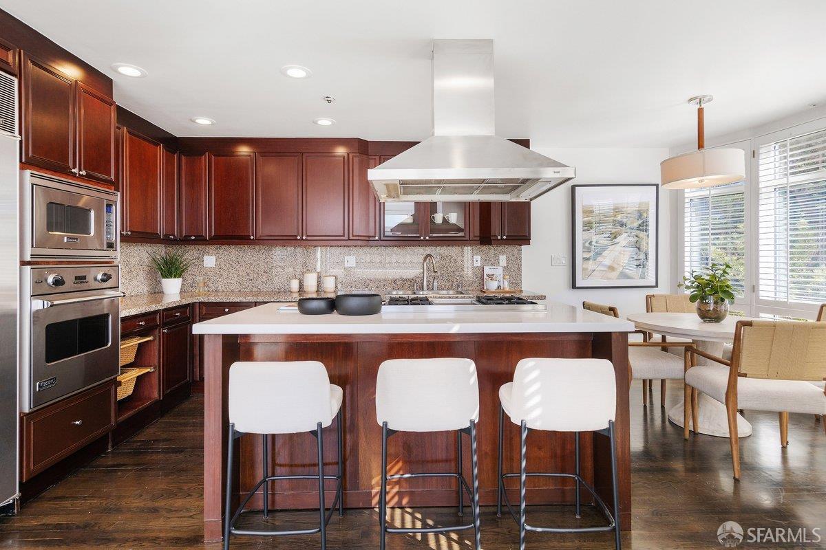 Kitchen with cherry cabinets, stainless-steel appliances, and a large island with white stools.