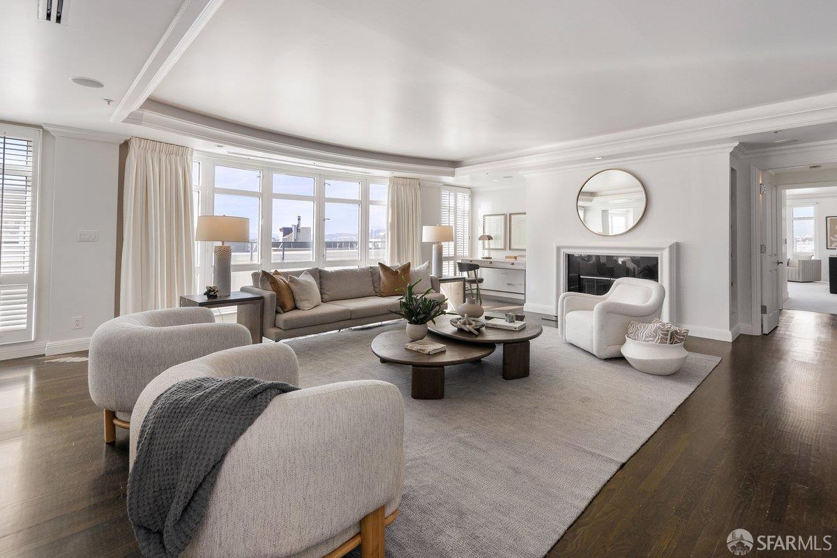 Living room with a fireplace, neutral seating, broad windows, and hardwood floors.