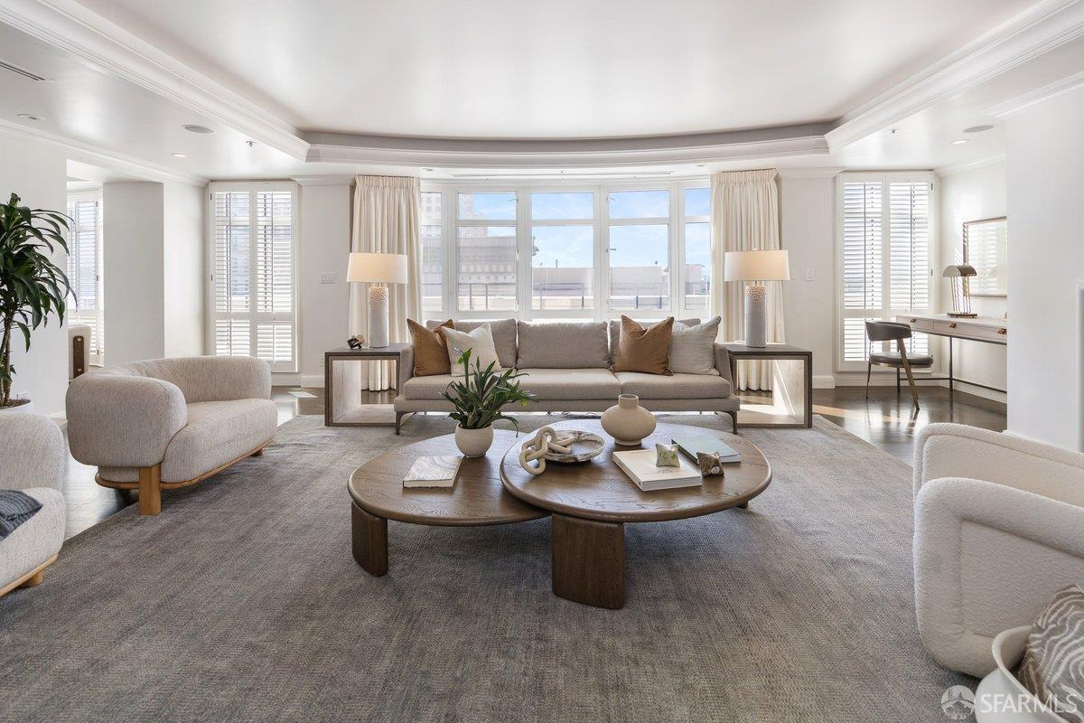 Living room with a gray sofa, round wooden coffee table, and large shuttered windows.
