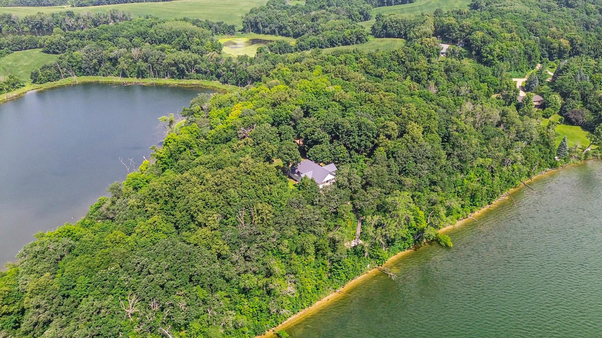 Aerial view of a wooded lakeside home on a peninsula between two bodies of water.