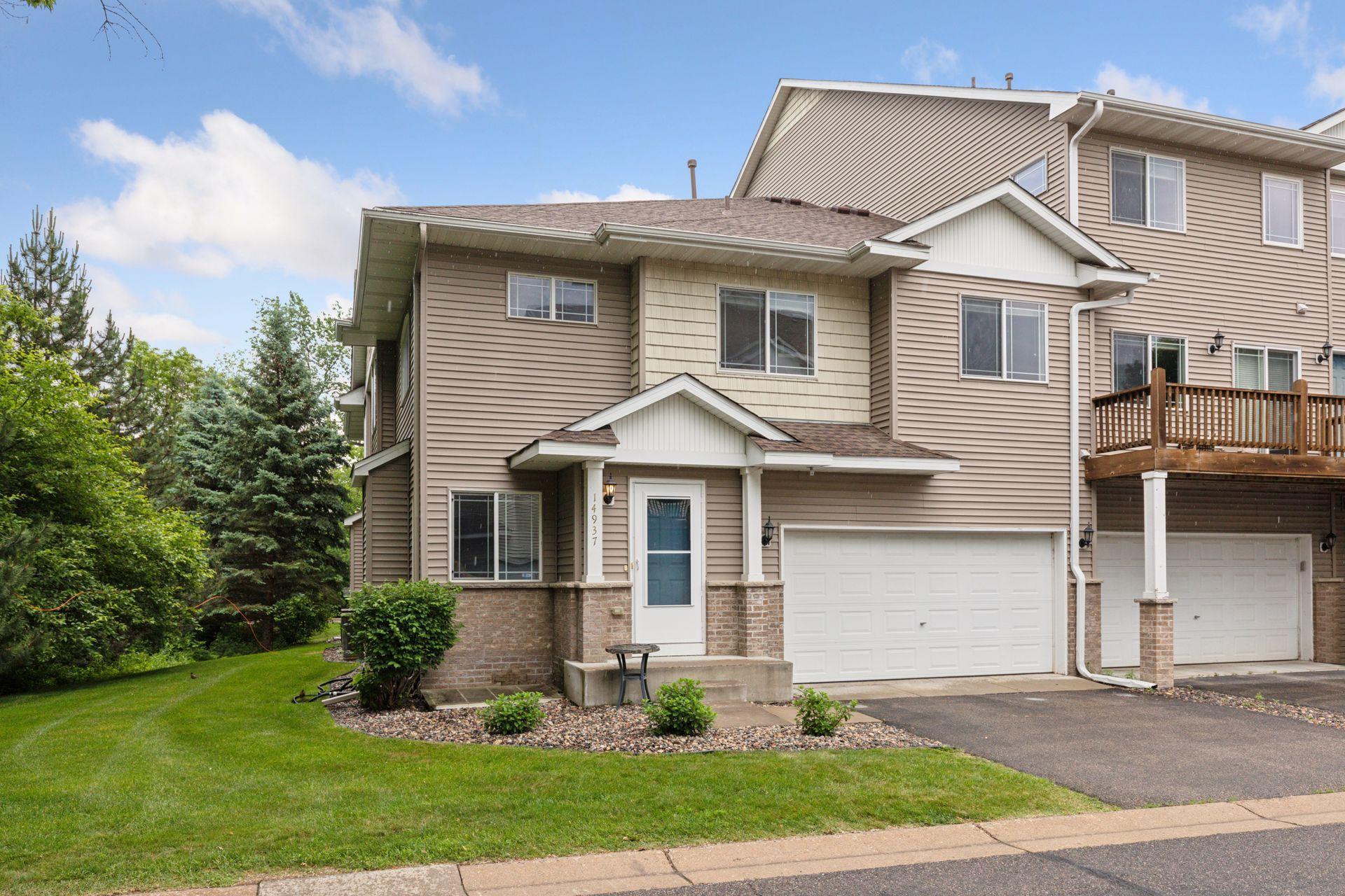 Tan-sided townhome with a blue front door, double garage, and neighboring raised deck.