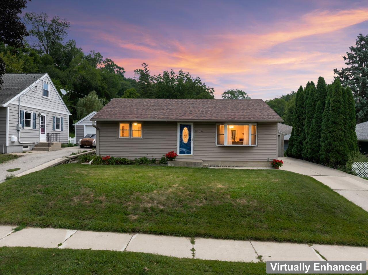 Single-story gray house with a blue front door and warmly lit windows at dusk.