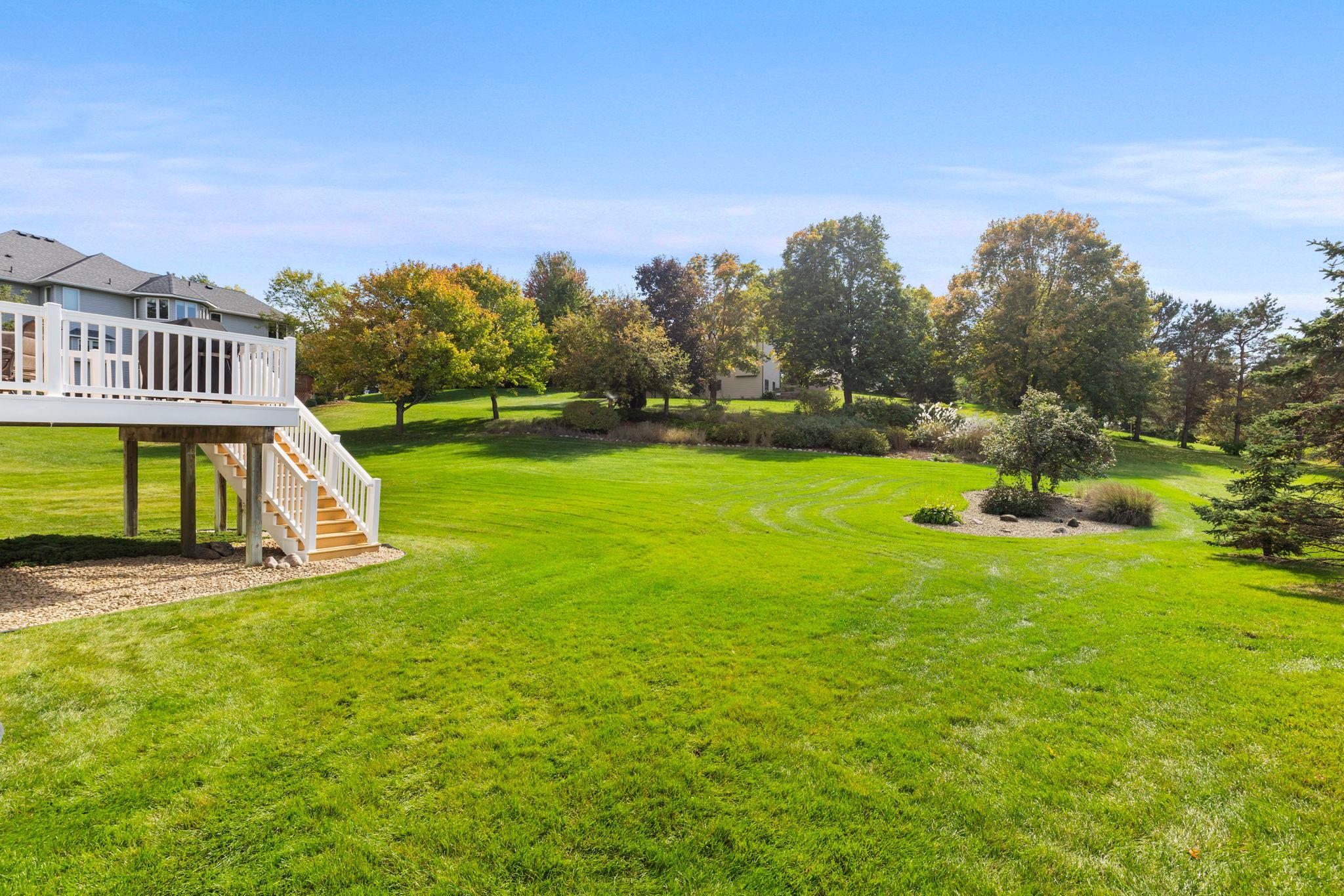 Spacious backyard lawn with mature trees and a raised deck with white stairs.