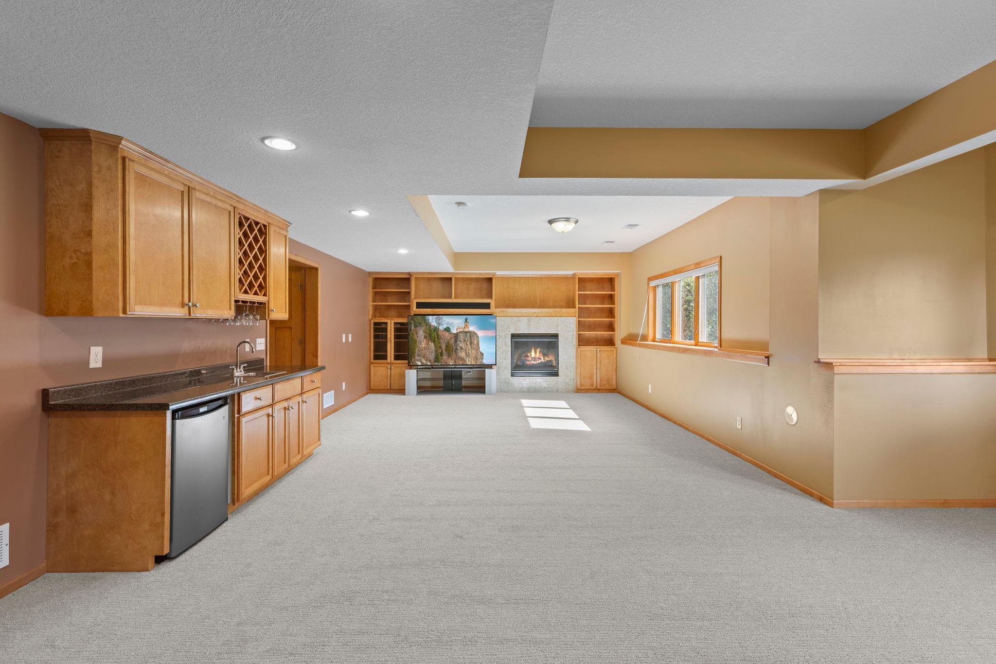 Basement recreation room with a built-in wet bar, fireplace, and extensive wood cabinetry.