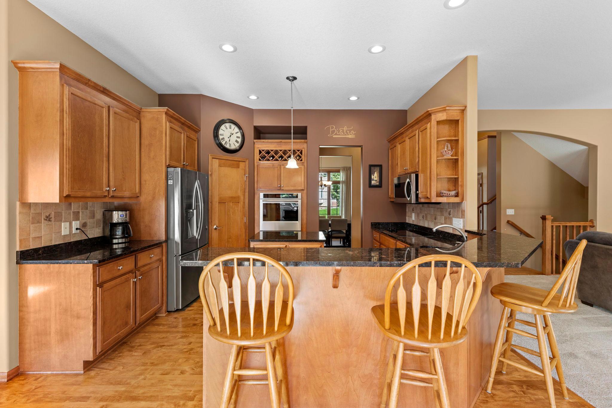 Kitchen with warm wood cabinets, granite island, stainless steel appliances, and wooden bar stools.