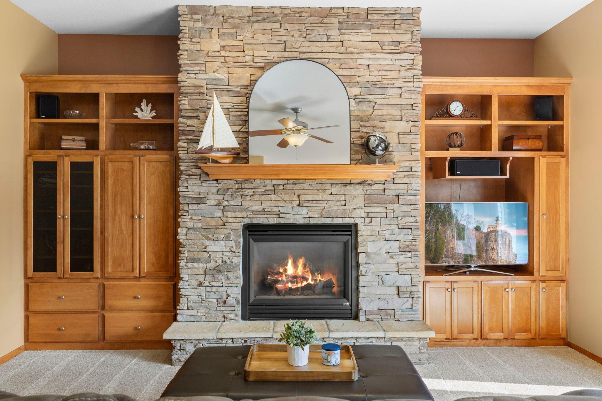 Living room with a lit stone fireplace, arched mirror, and built-in wooden cabinets.