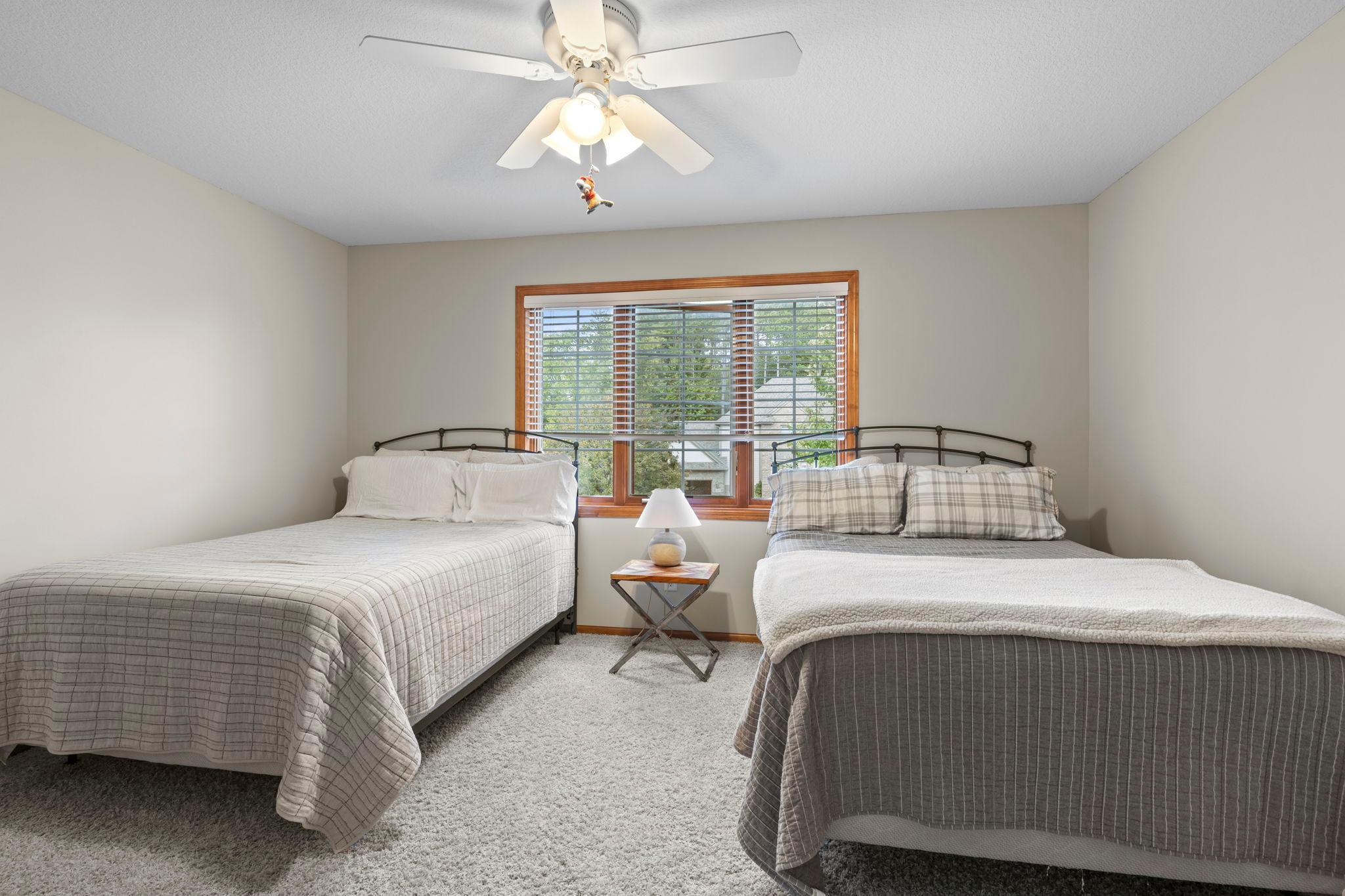 Bedroom with two beds and a wide wood-trimmed window overlooking trees.