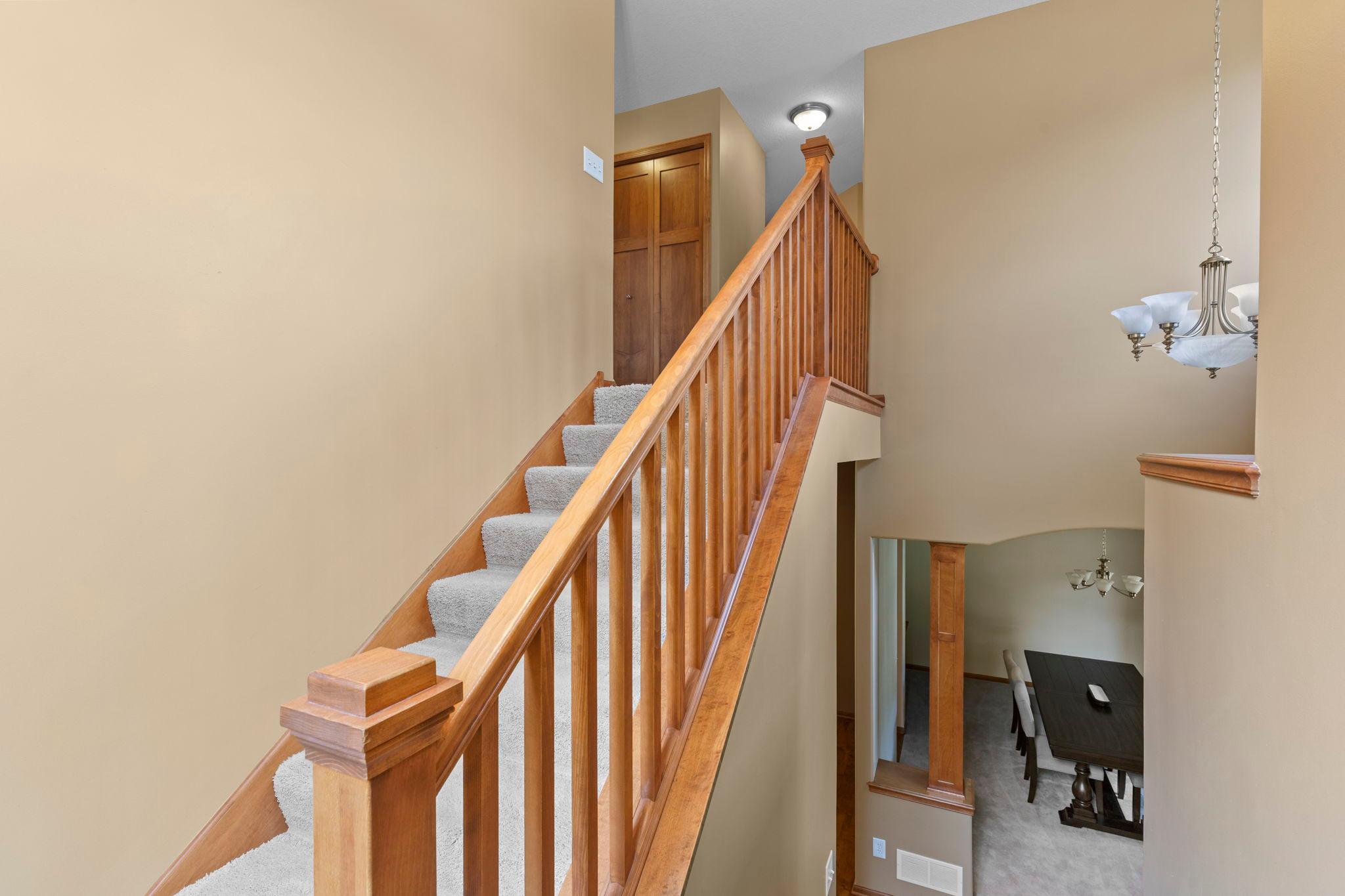 Two-story foyer with carpeted stairs, a wooden railing, and a view of the dining area below.