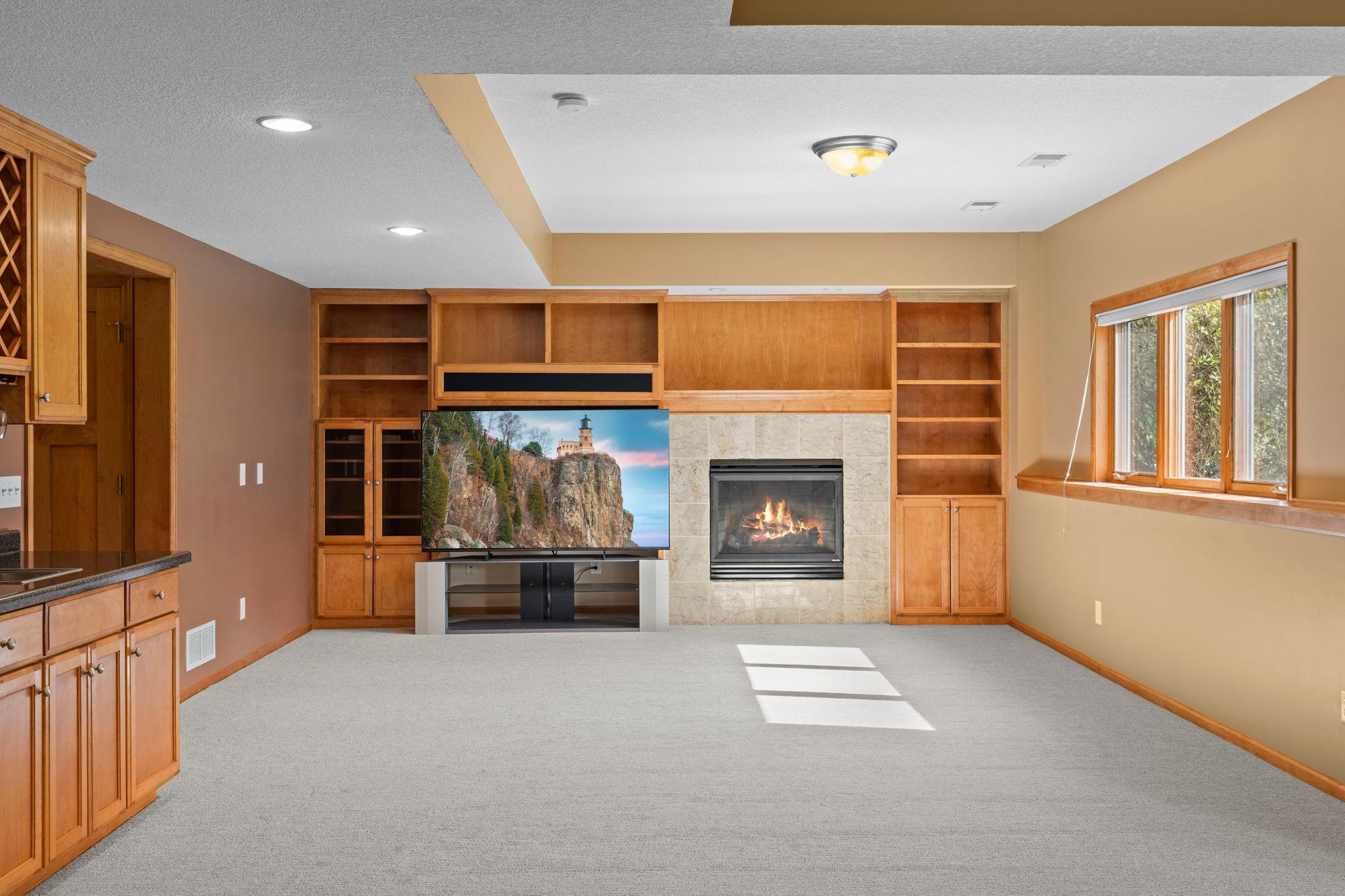 Living room with built-in wood shelving, a tiled fireplace, and a large window.