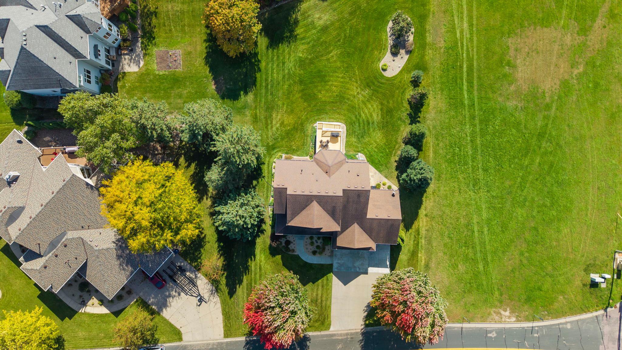 Aerial view of a home with a broad lawn, landscaped trees, and neighboring houses.