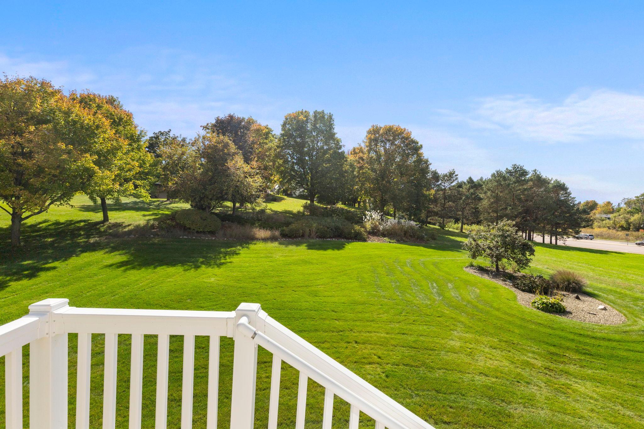 Spacious lawn and landscaped yard with mature trees, seen from a white deck railing.