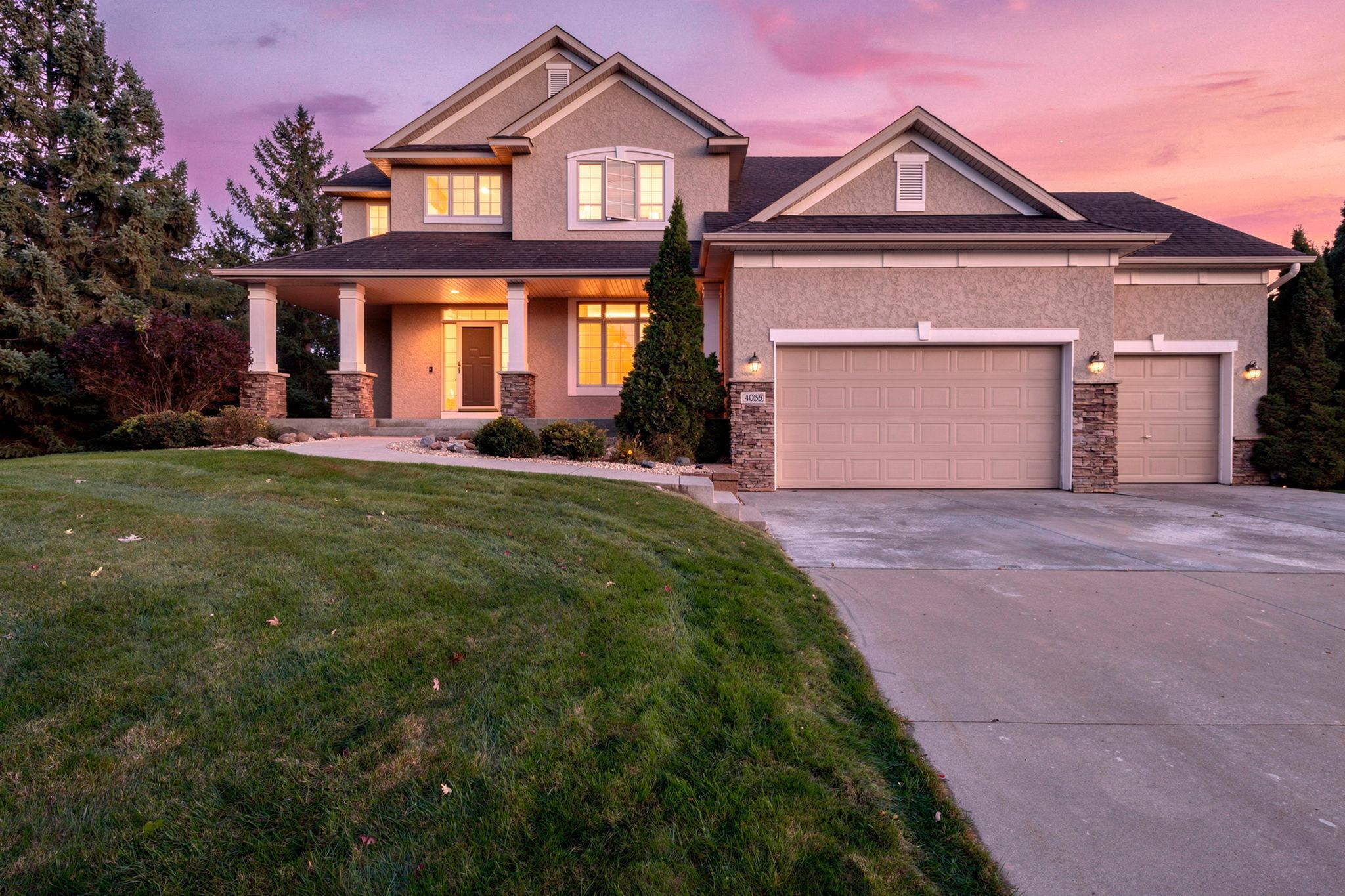 Two-story stucco home with a covered porch and three-car garage at dusk.