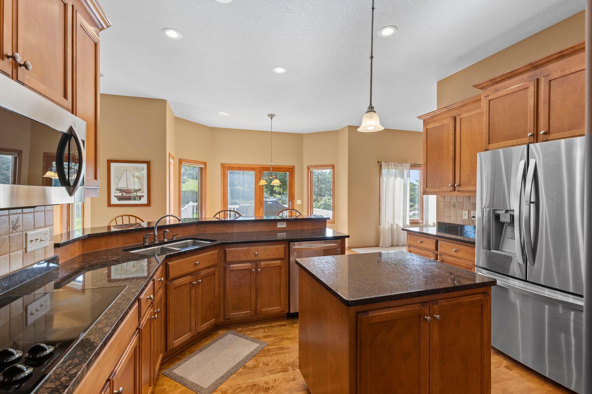 Kitchen with warm wood cabinets, dark stone counters, a central island, and stainless steel appliances.