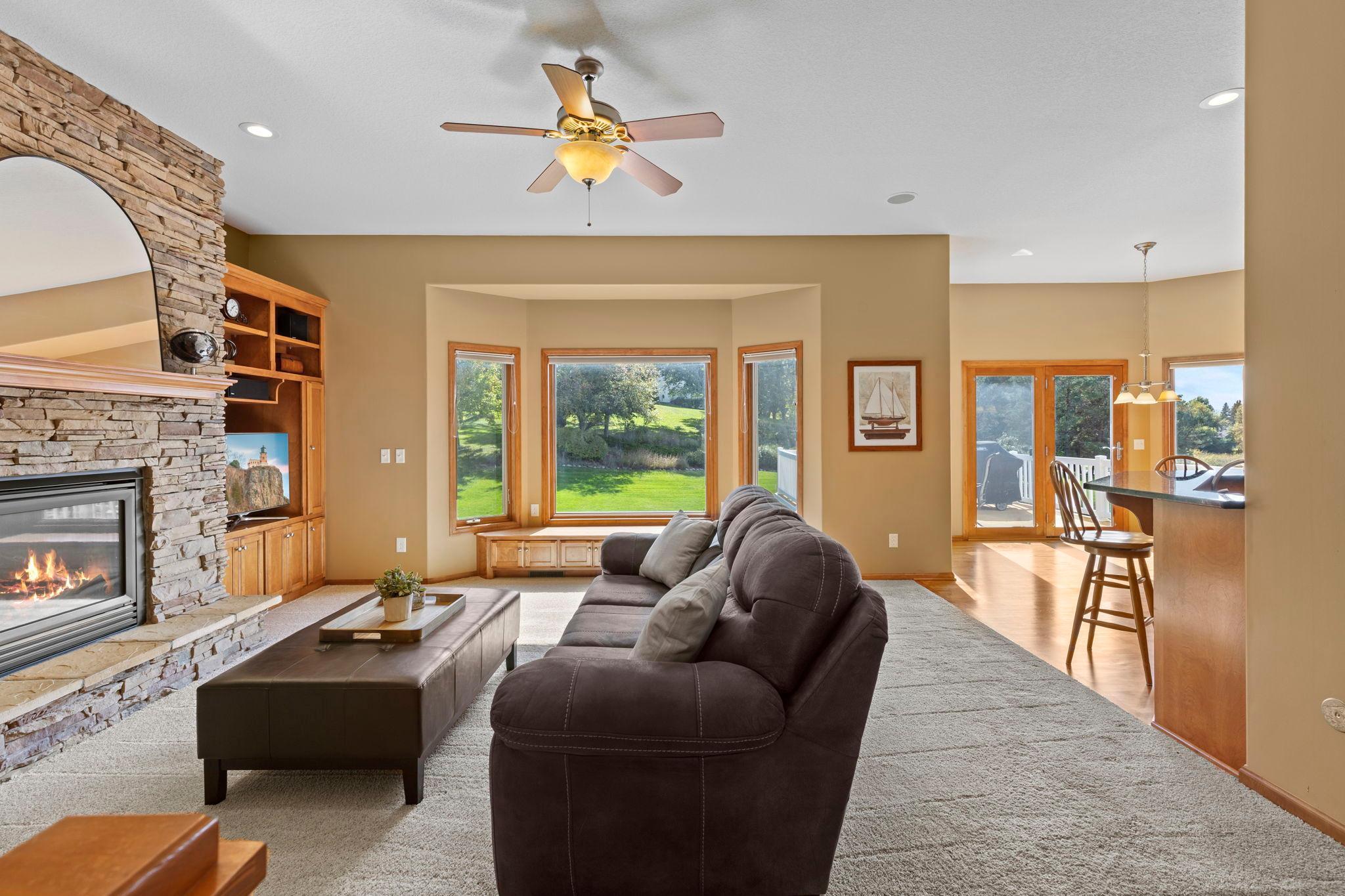 Living room with a stone fireplace, built-in cabinetry, and wide windows overlooking the yard.