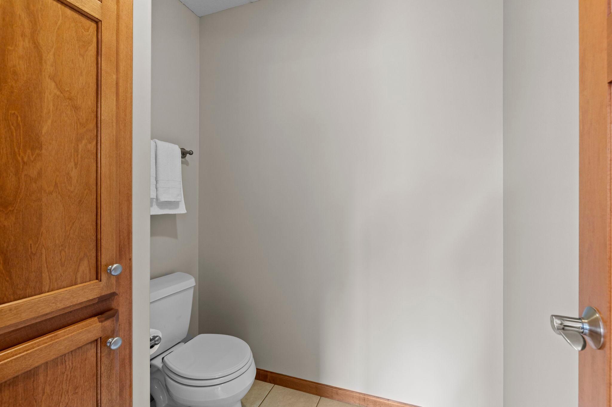 Small bathroom with a white toilet, folded towels, and warm wood doors.