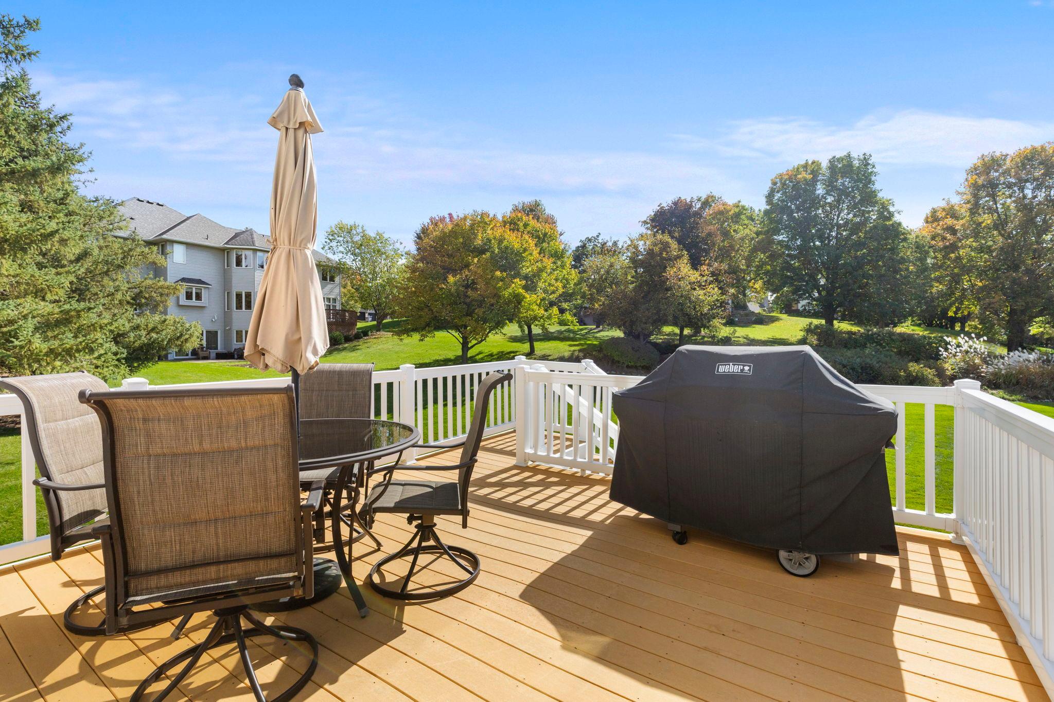 Outdoor deck with patio seating and a covered grill overlooking a leafy lawn.