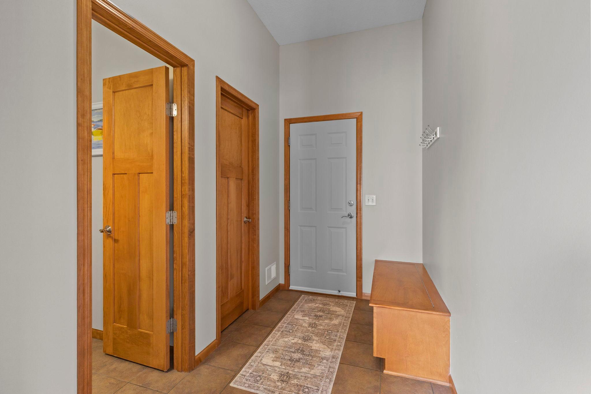 Entryway with a gray front door, wood-trimmed doors, tiled floor, and patterned runner.