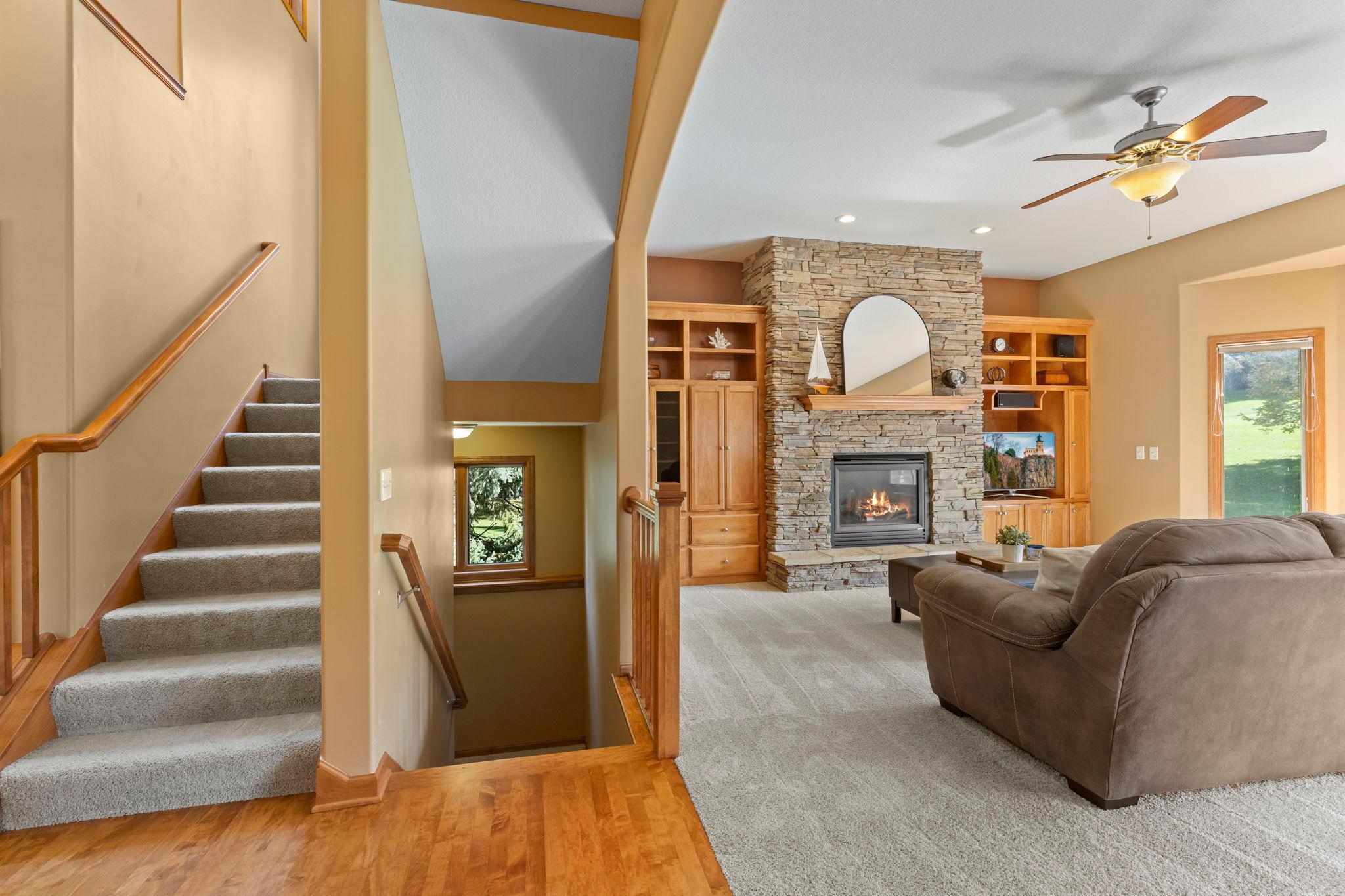 Living room with a stone fireplace, built-in wooden shelves, and a carpeted staircase.