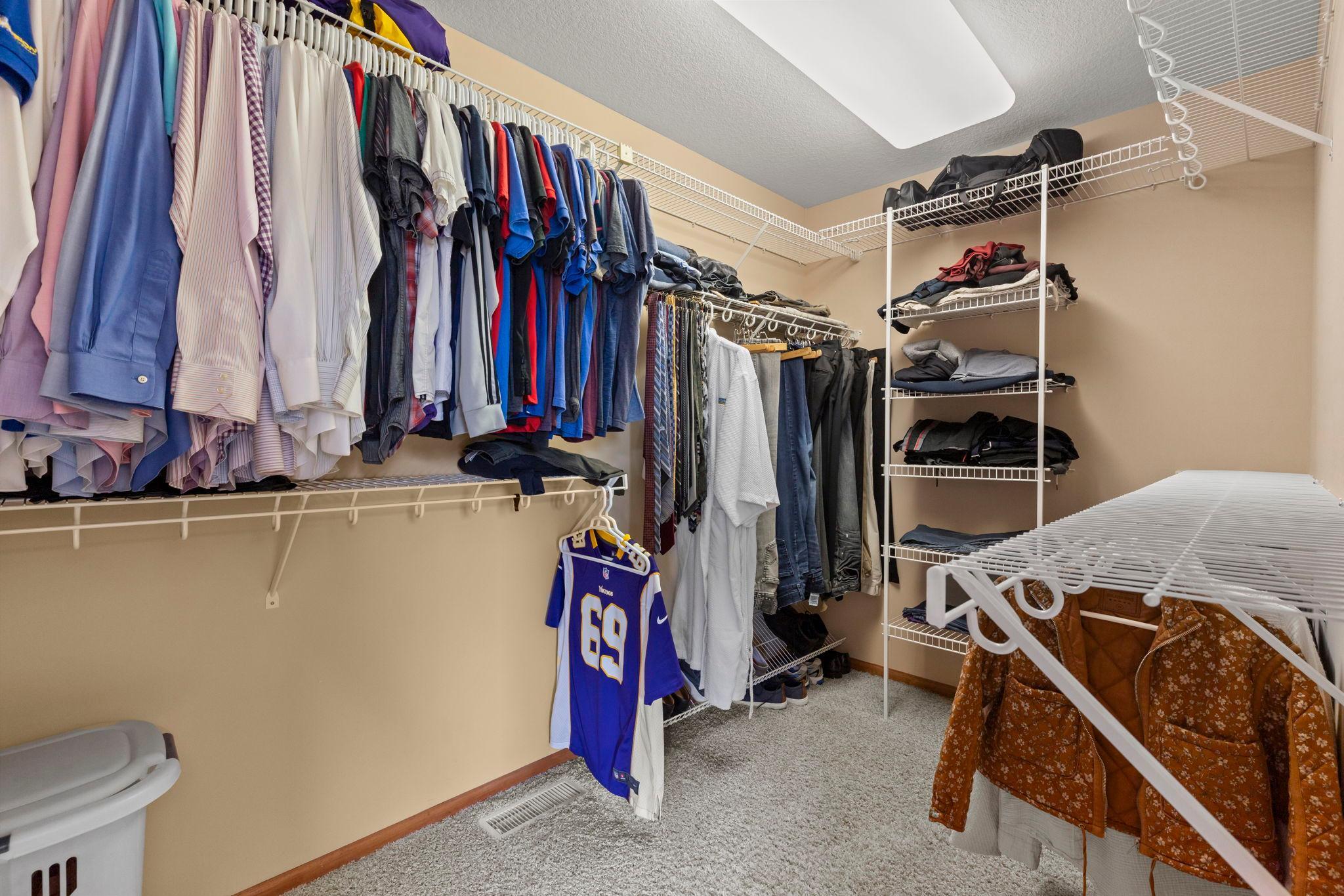 Walk-in closet with extensive wire shelving, hanging clothes, folded garments, and carpeted floor.
