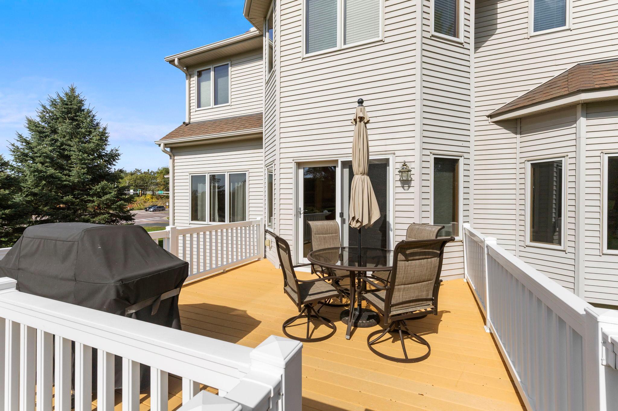 Raised wood deck with white railings, outdoor dining set, closed umbrella, and covered grill.