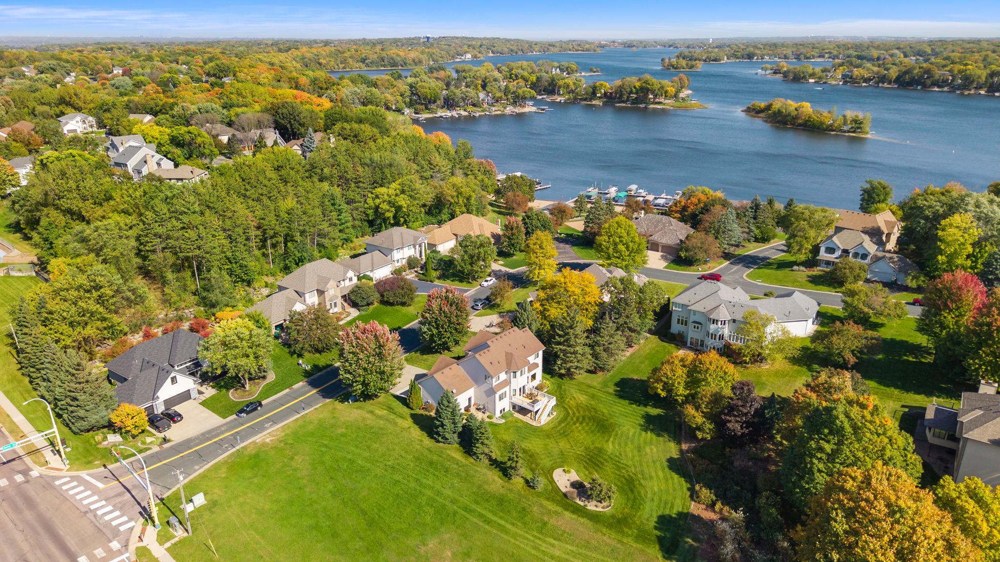 Aerial view of a lakeside neighborhood with autumn foliage, docks, and wooded islands.