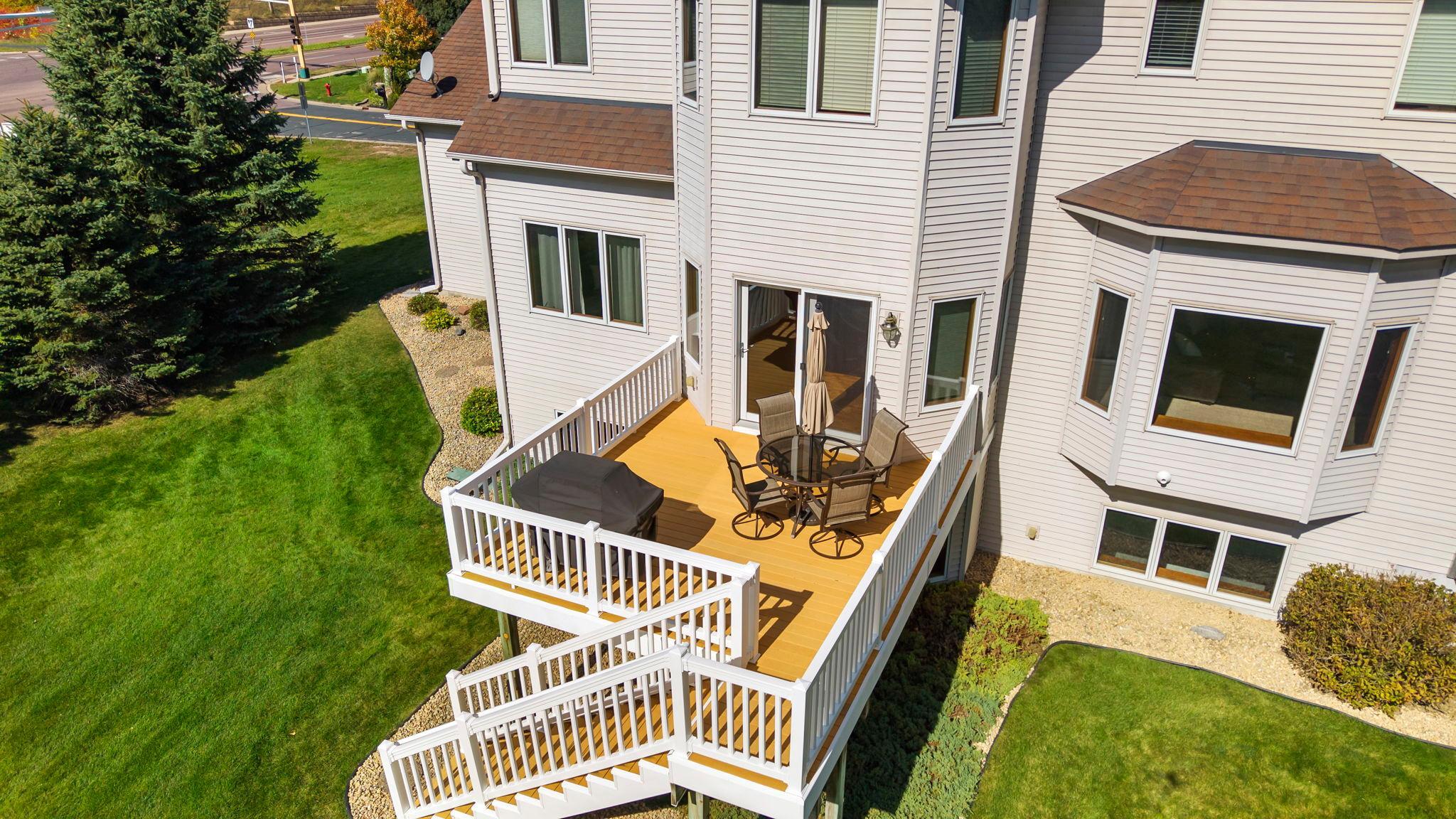Raised deck with white railings, outdoor dining set, and covered grill beside a two-story home.