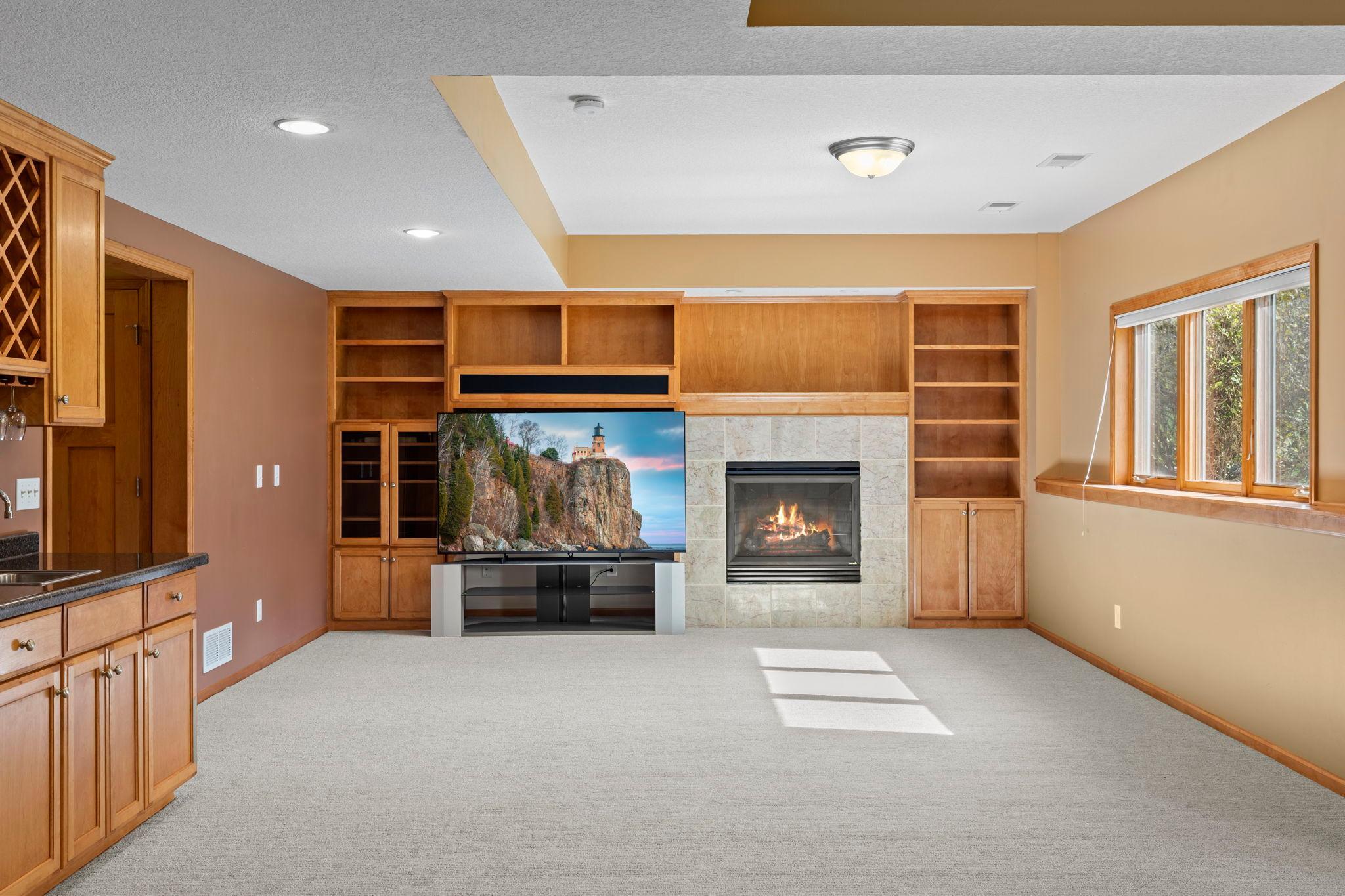 Living room with built-in wood shelving, a stone fireplace, and sunlight across the carpet.