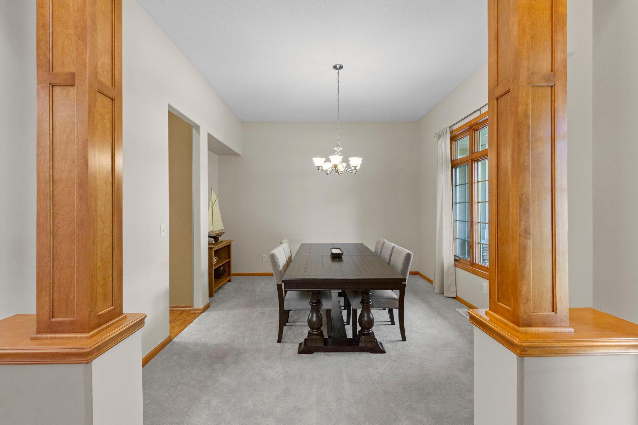 Dining room with a dark wood table, chandelier, gray carpet, and large wood-trimmed windows.