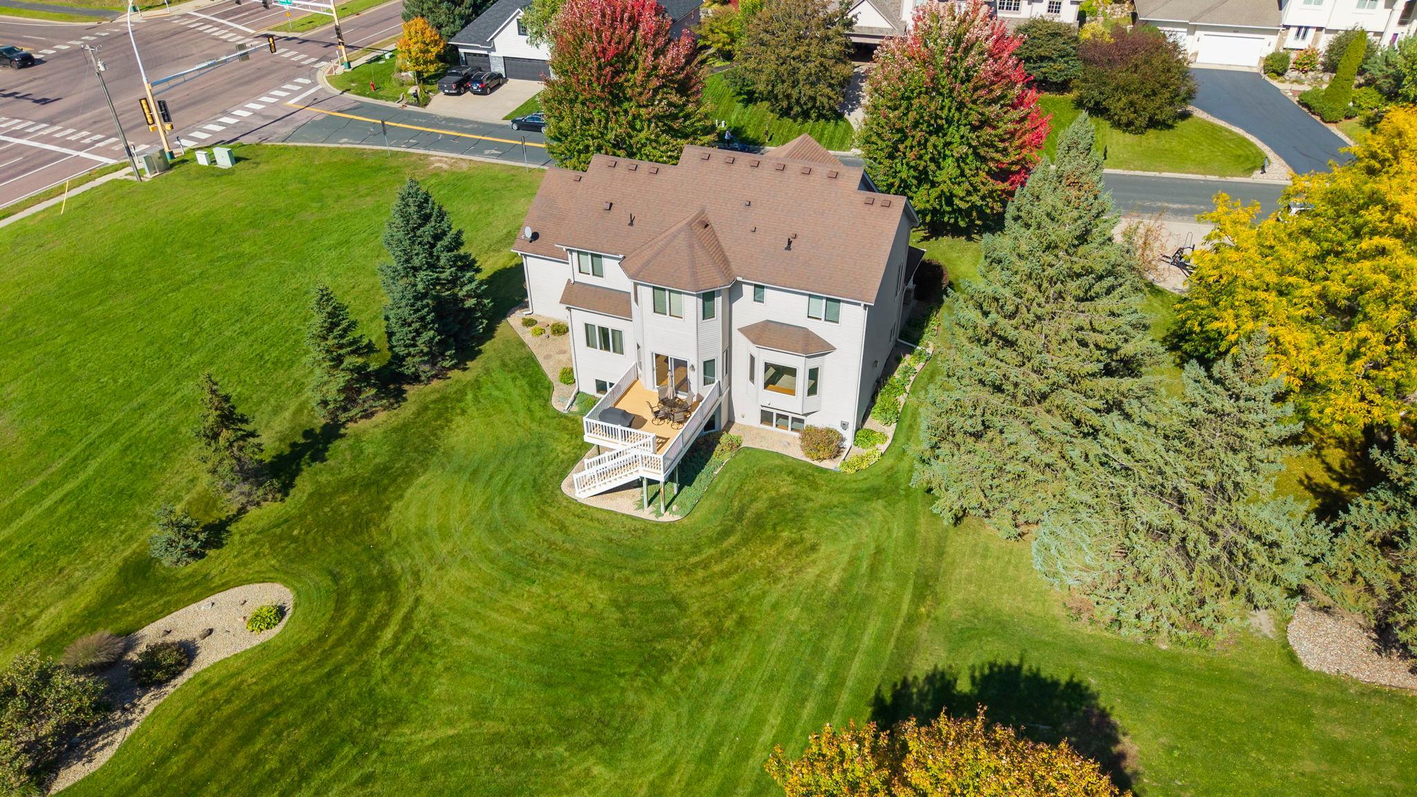 Aerial view of a white two-story house with a raised deck, broad lawn, and mature autumn trees.