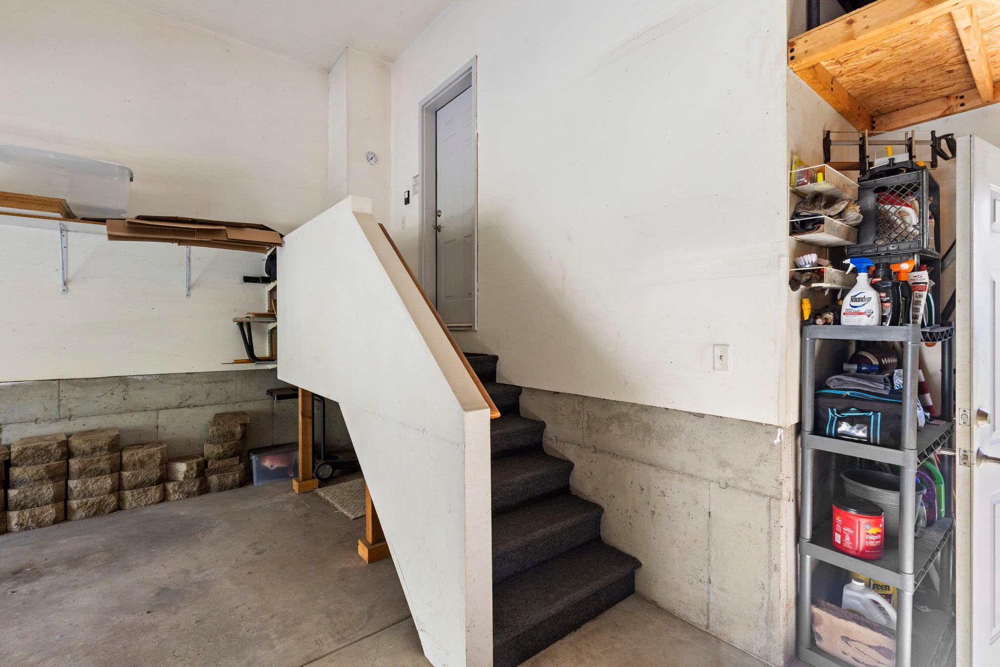 Garage with carpeted stairs leading to a gray door, concrete block walls, and storage shelves.