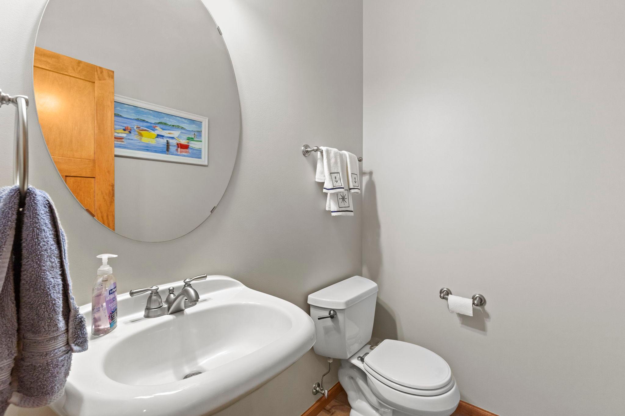 Bathroom with a white sink and toilet, round mirror, and neatly hung towels.