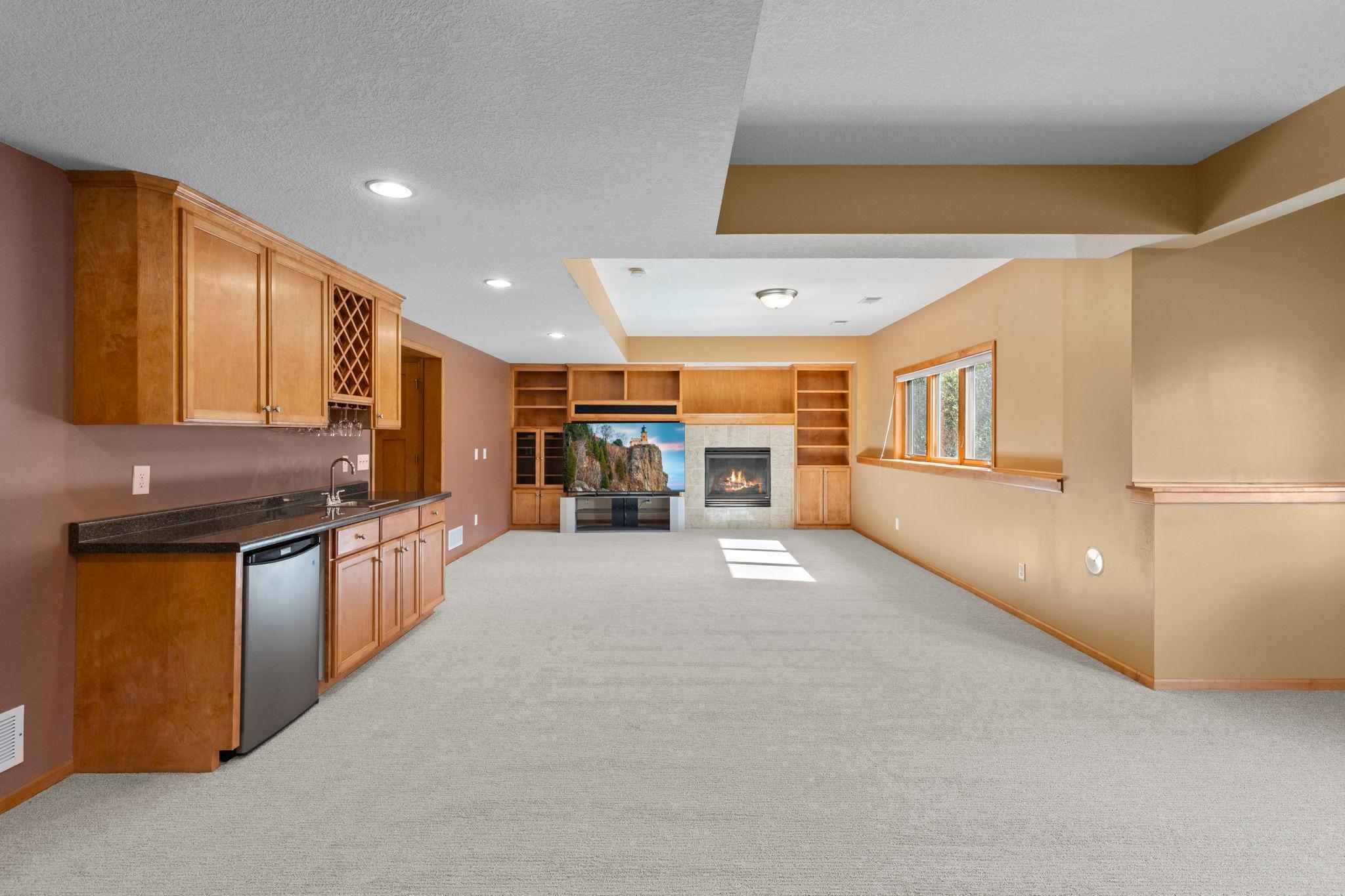 Carpeted living area with a built-in wet bar, fireplace, wooden shelving, and wide window.