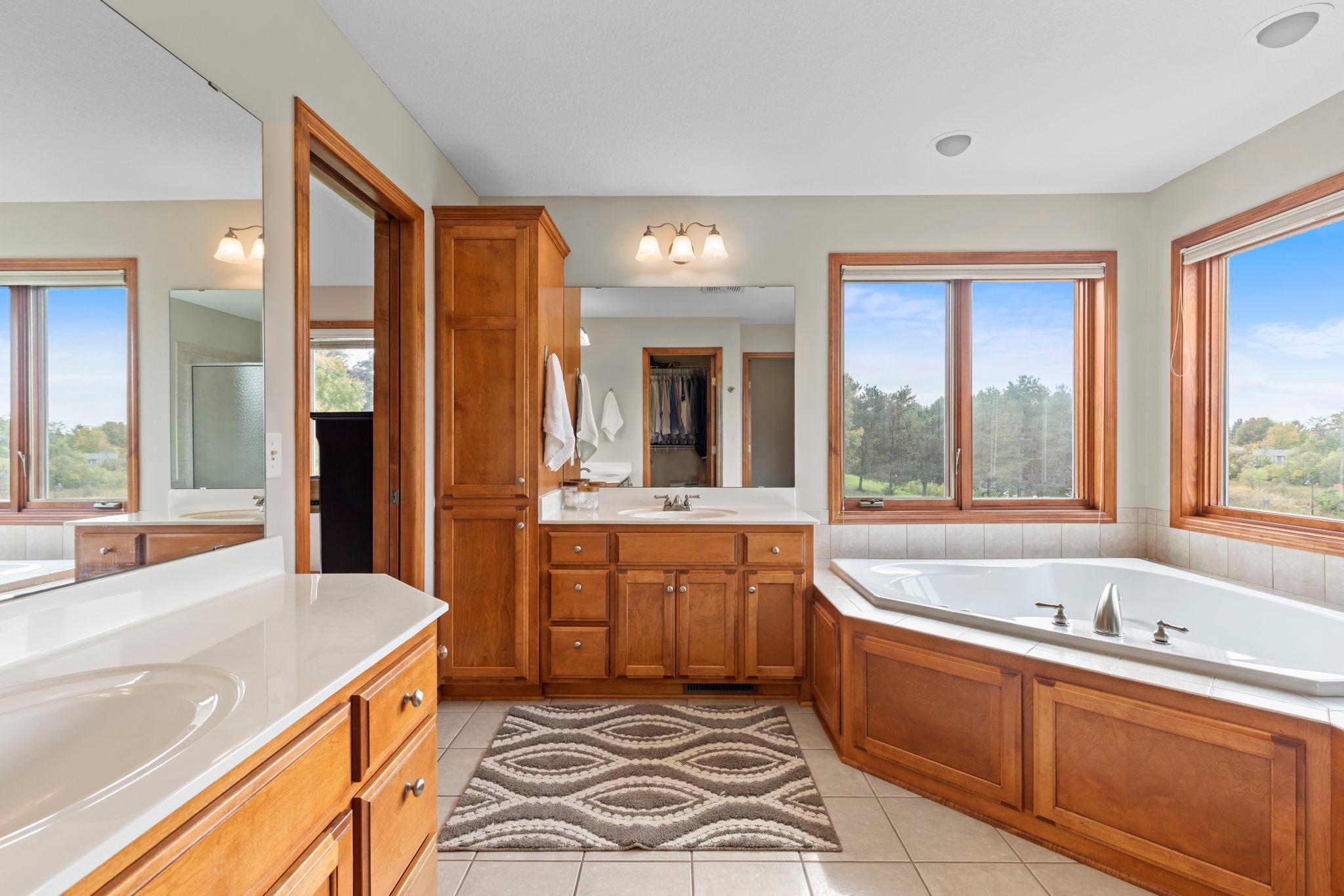 Spacious bathroom with warm wood vanities, a built-in soaking tub, and large windows.