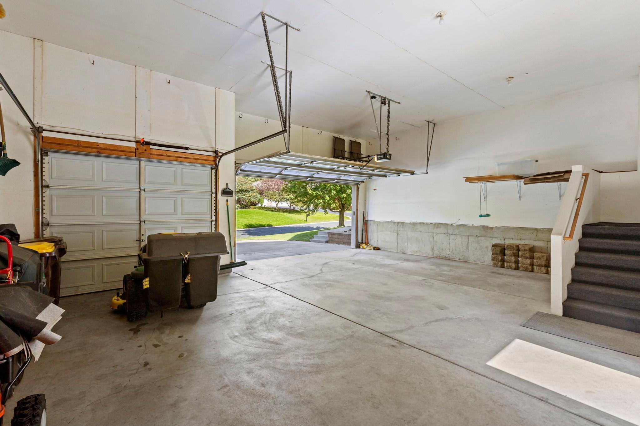 Spacious garage with two doors, concrete floor, storage shelves, and a staircase.
