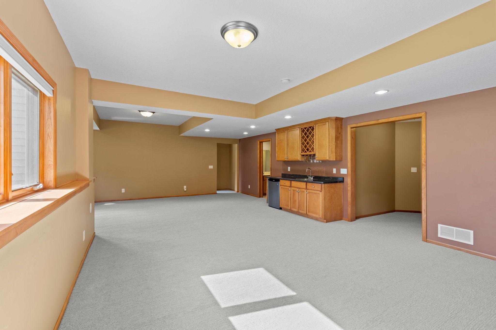 Unfurnished basement with carpet, wood-trimmed window, and built-in wet bar with wine rack.