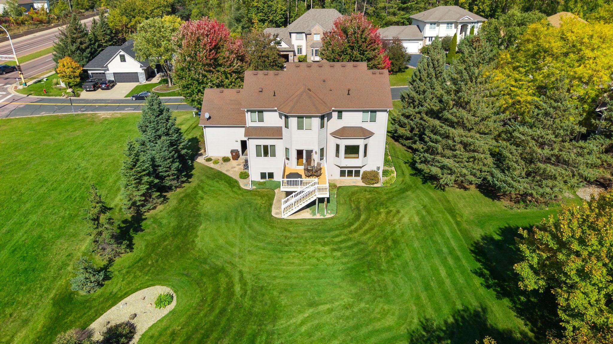 Aerial view of a two-story home, deck, and expansive lawn bordered by mature trees.