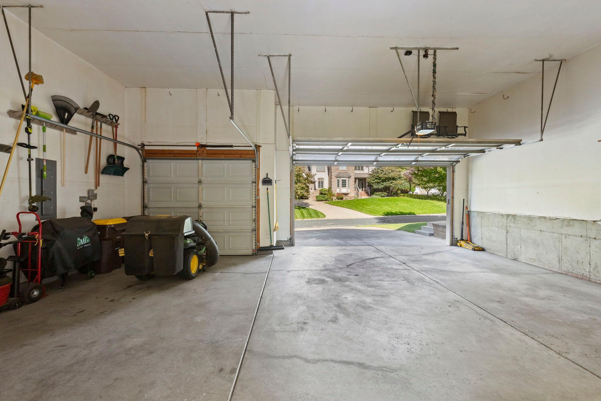 Spacious garage with garden tools and lawn equipment, viewed toward an open door and driveway.