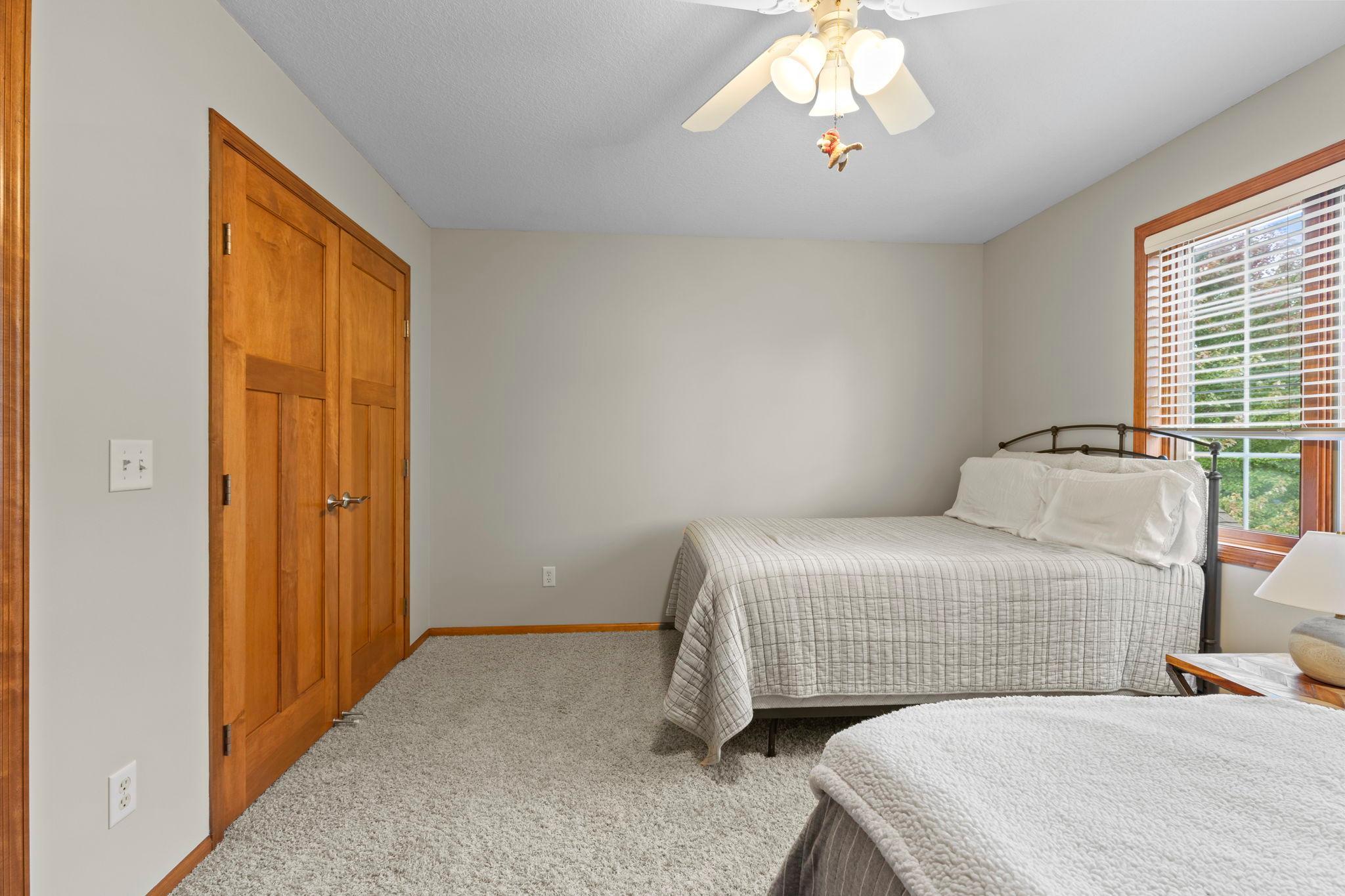 Bedroom with a metal-frame bed, warm wood closet doors, and a large window with blinds.