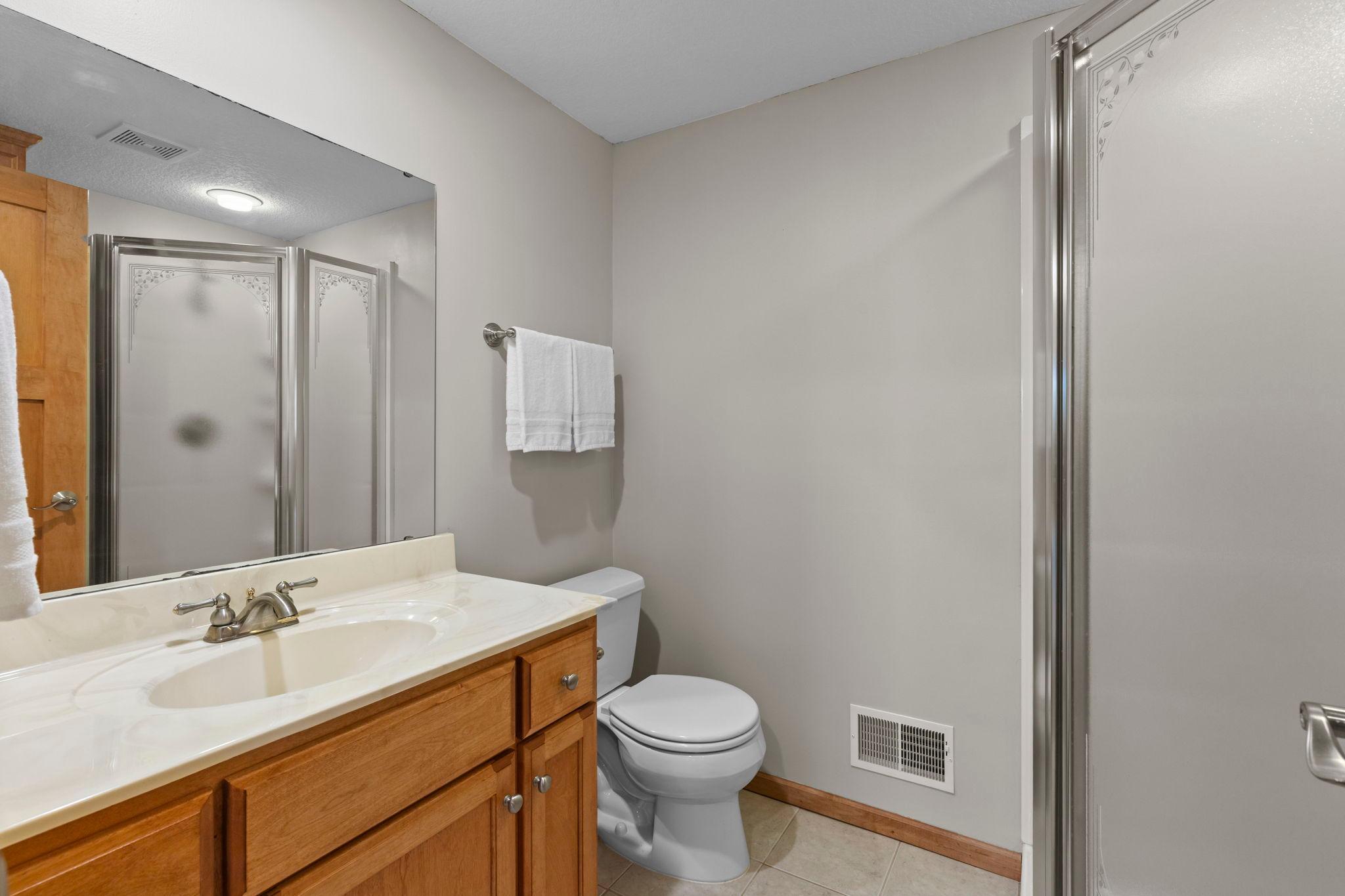 Bathroom with a wood vanity, large mirror, toilet, and glass shower enclosure.