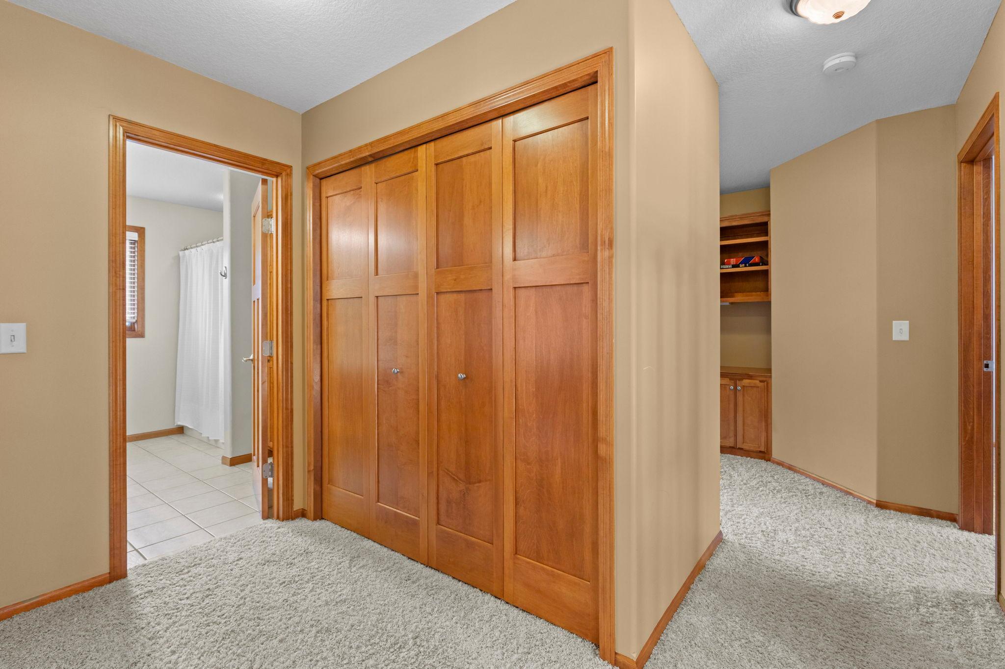 Hallway with wood-paneled closet doors, a tiled bathroom entrance, and built-in shelving.