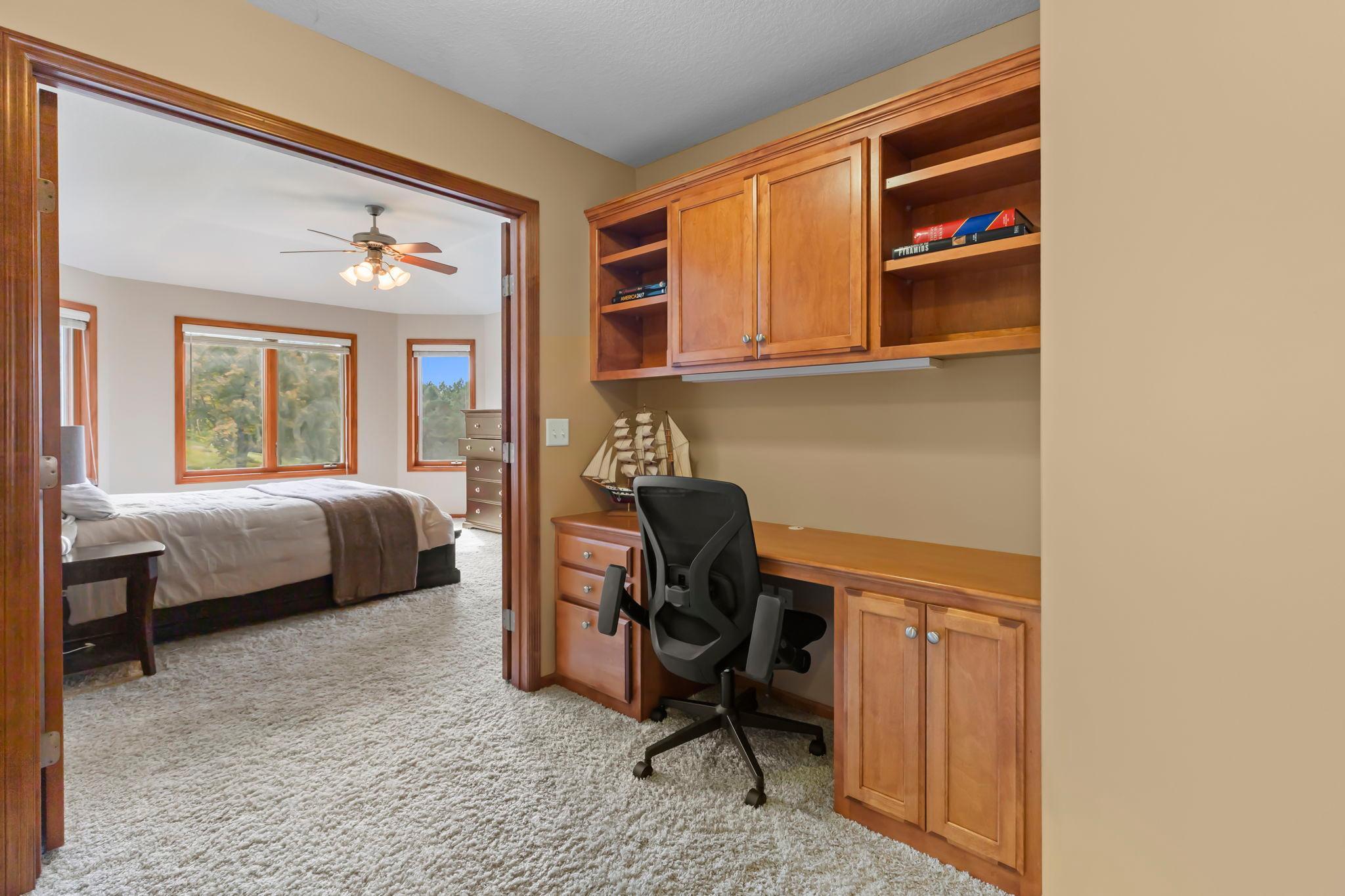 Built-in wood home office with desk and chair, opening into a carpeted bedroom.