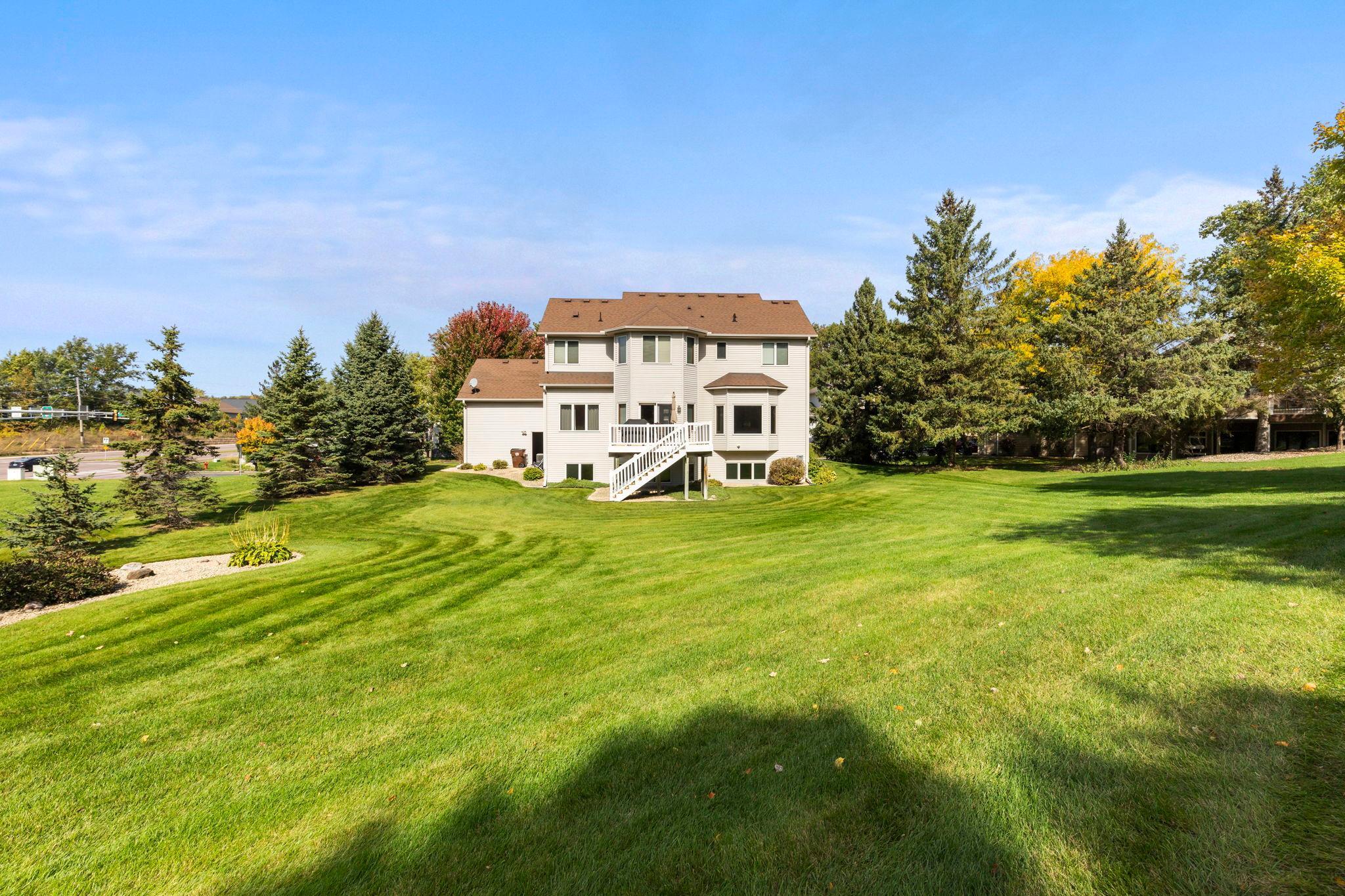Rear of a two-story house with deck stairs overlooking a broad lawn and autumn trees.