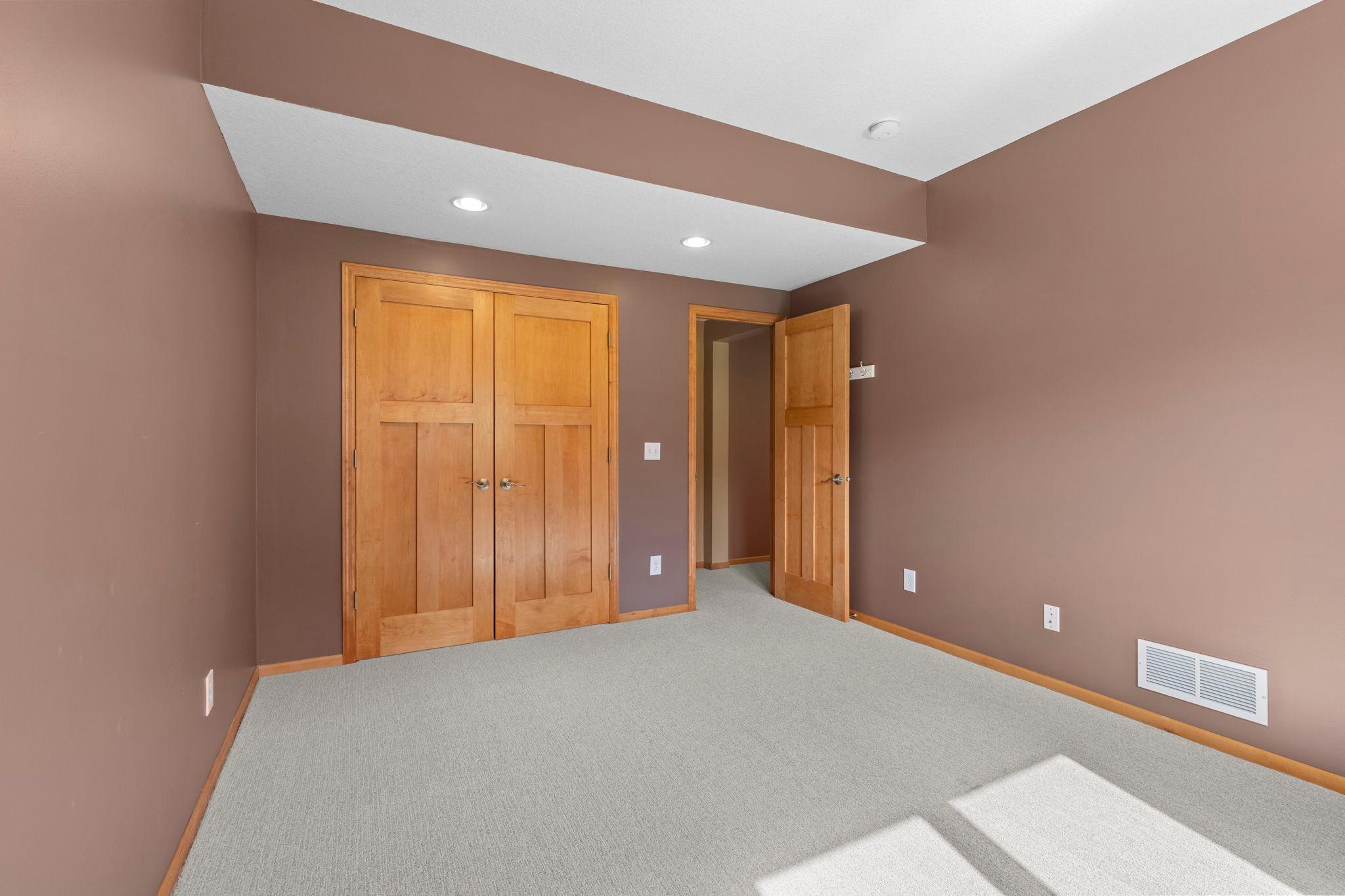Empty carpeted bedroom with double wooden closet doors and sunlight across the floor.