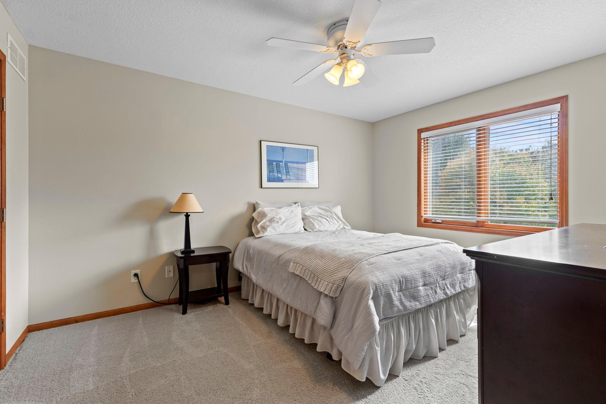 Bedroom with a white bed, ceiling fan, carpet, and a large wood-trimmed window.