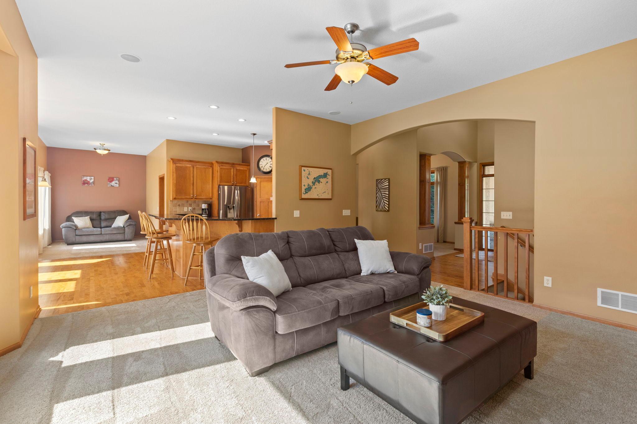 Open-plan living room with gray sectional, wood-floored dining area, and kitchen with wood cabinets.