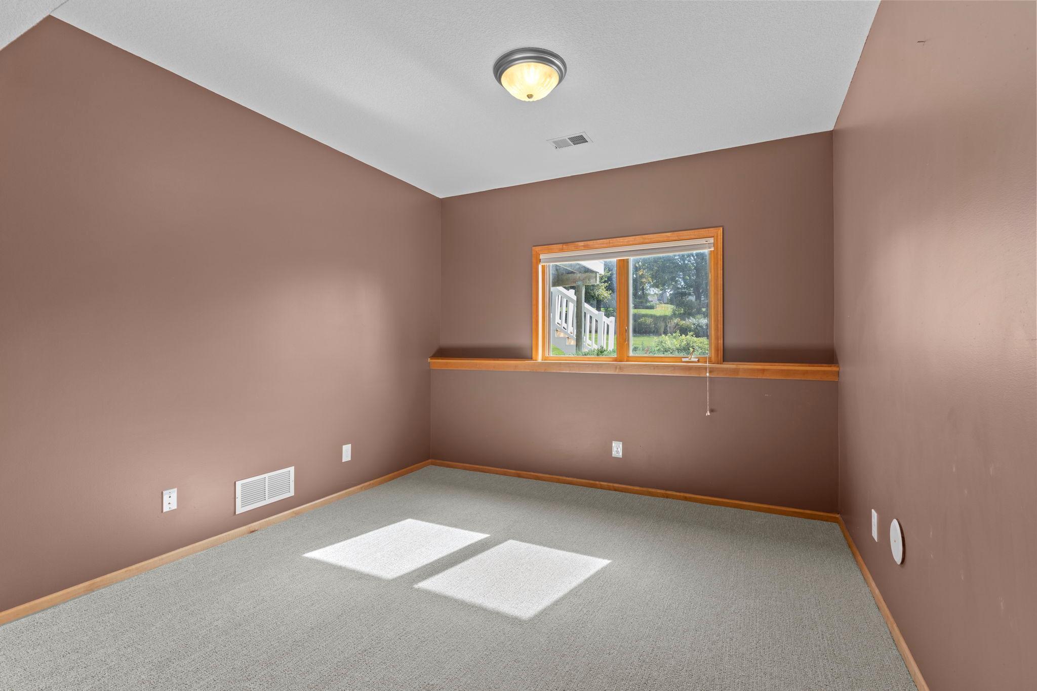 Empty carpeted room with brown walls, wood trim, and sunlight through a window.