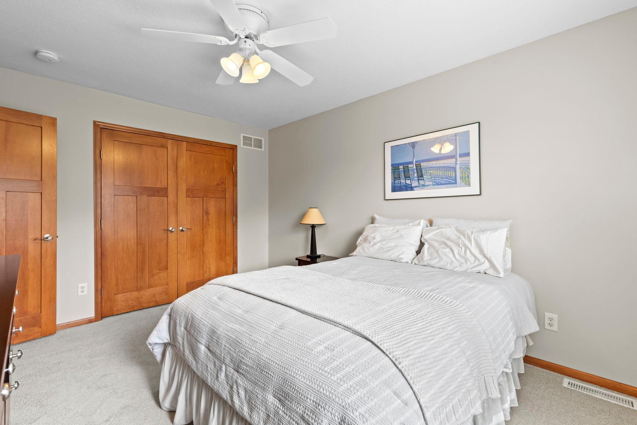 Bedroom with a white bed, warm wood closet doors, gray carpet, and ceiling fan.