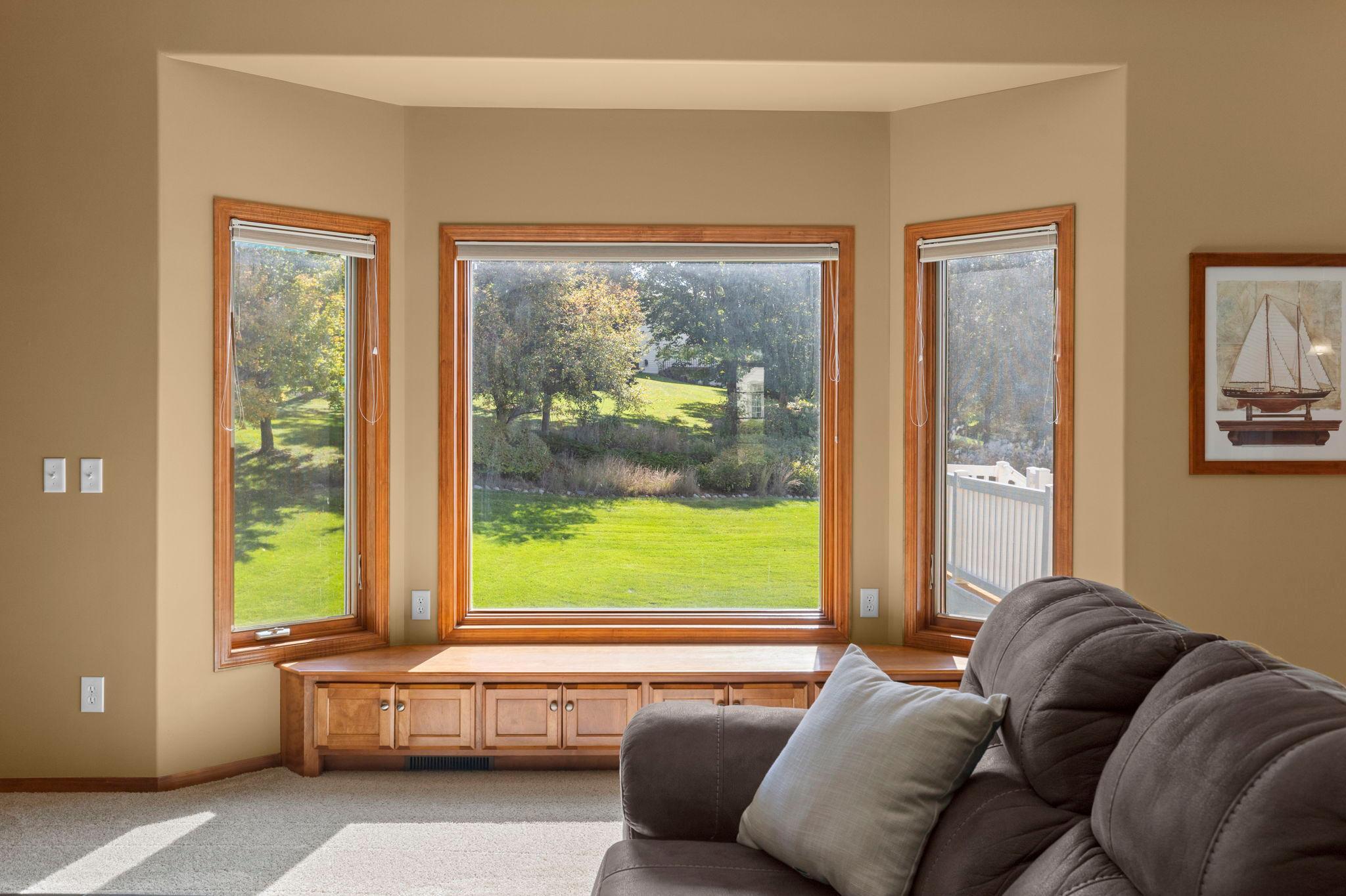 Living room with built-in wood window-seat cabinets and a view of the green lawn through three windows.