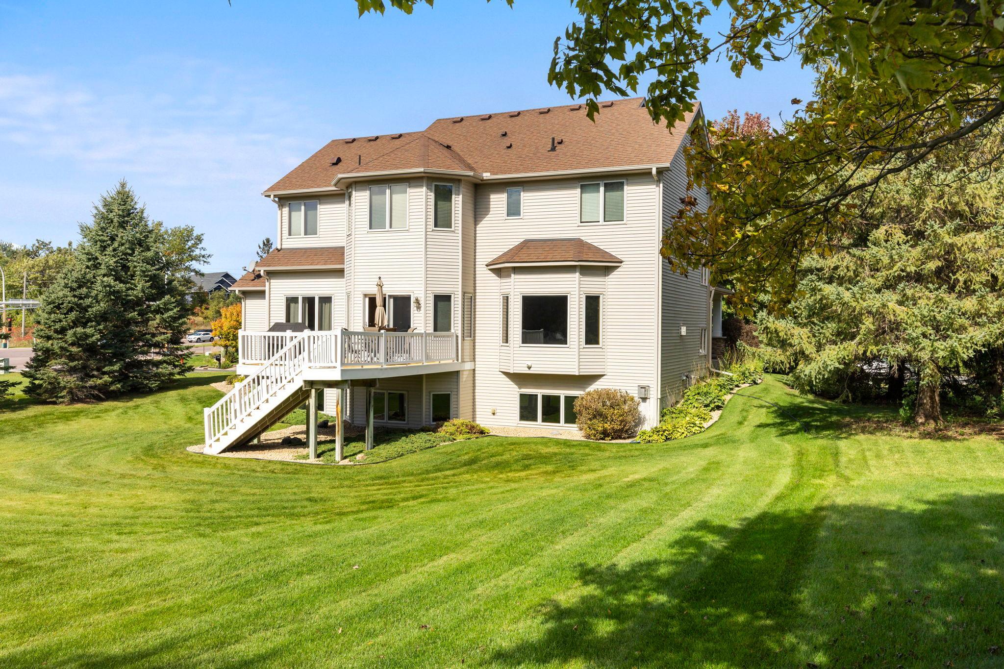 Two-story home's rear exterior with a white-railed deck, stairs, and expansive lawn.